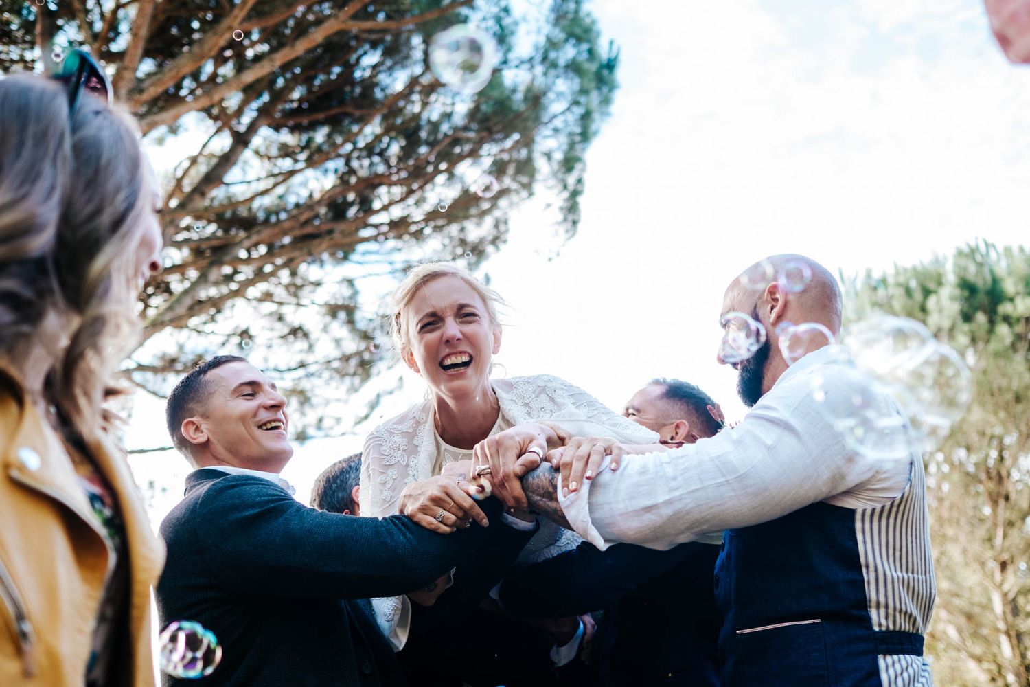 Wedding guests celebrate by raising their hands in joyful excitement during an outdoor ceremony.