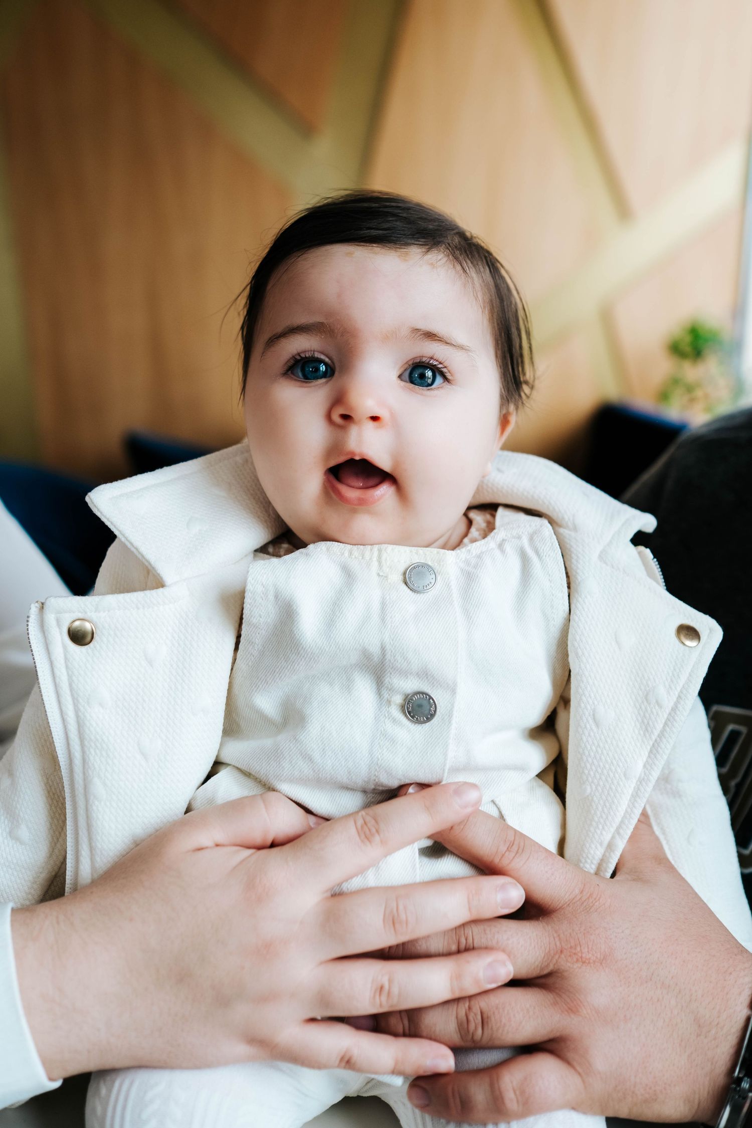 A series of close-up shots showing a baby in a white outfit being held against a warm-toned background.