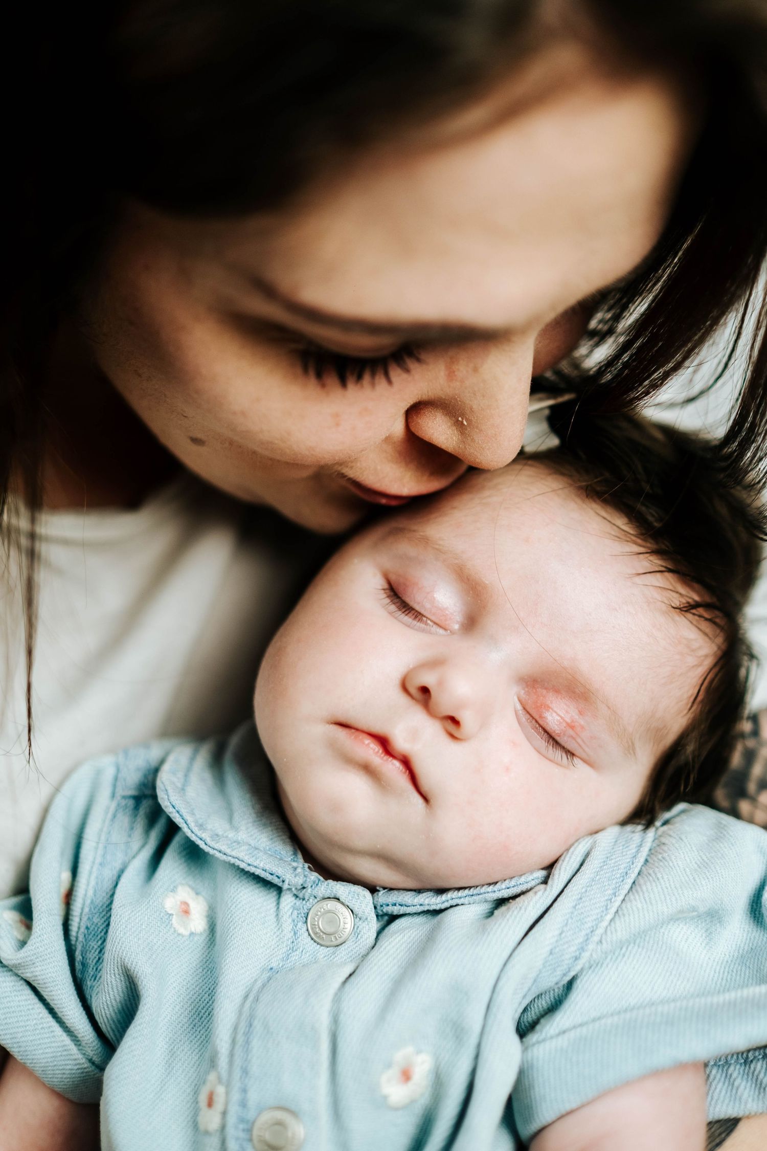 A tender moment captured as a sleeping baby in light blue clothing receives a gentle kiss and embrace.