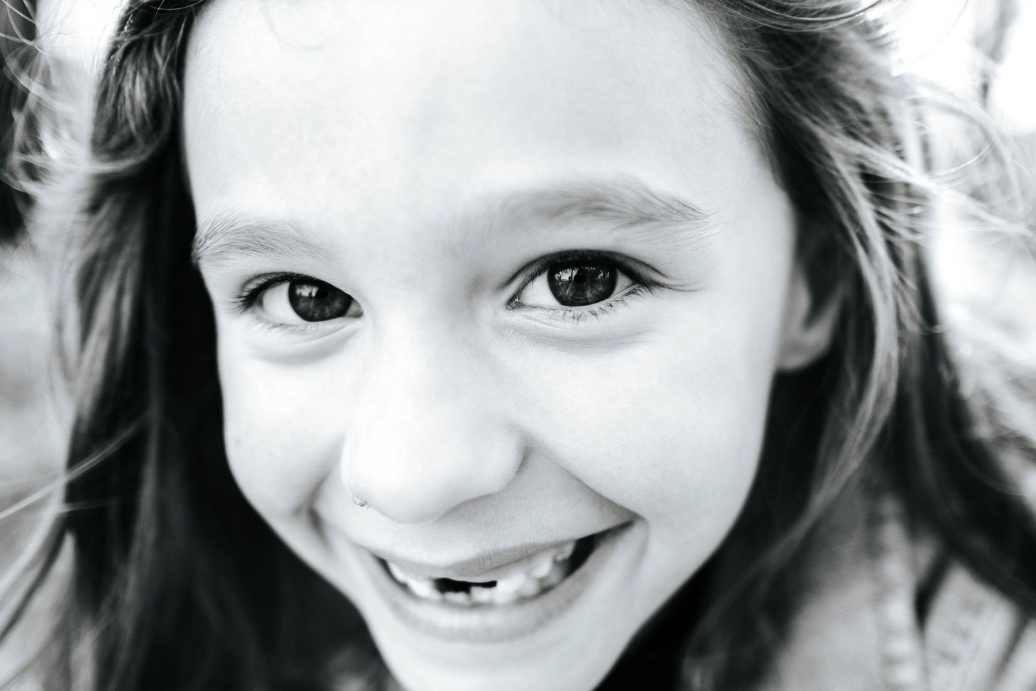Black and white close-up portrait of a smiling young girl with missing front teeth and long dark hair.
