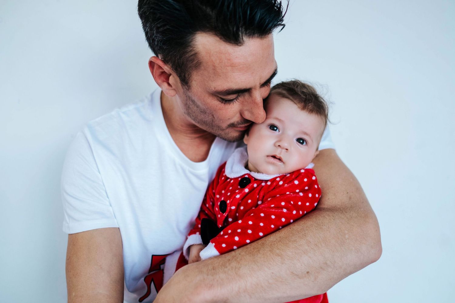 A parent in a white shirt holds a small baby wearing a red polka dot dress in a series of tender moments.