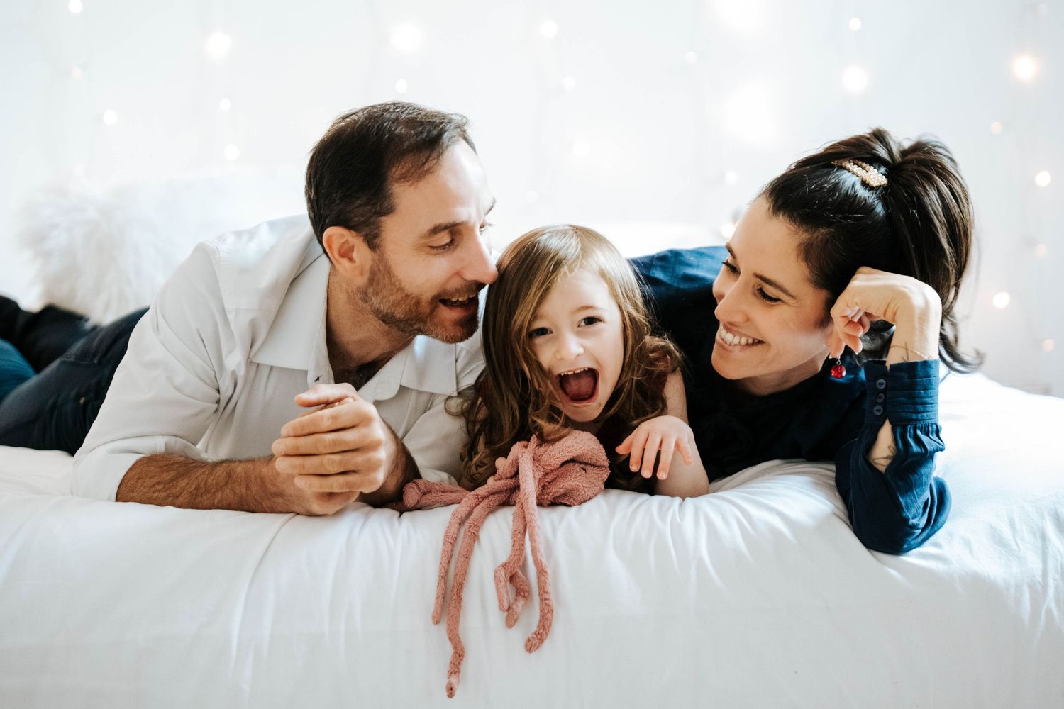 Family lying together on white bedding sharing joyful laughter and smiles.