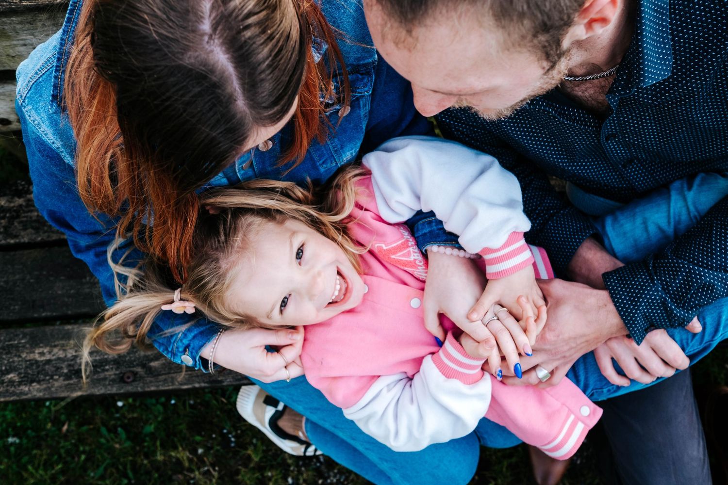 Parents laughing and cuddling their happy toddler girl outdoors in a joyful family moment.
