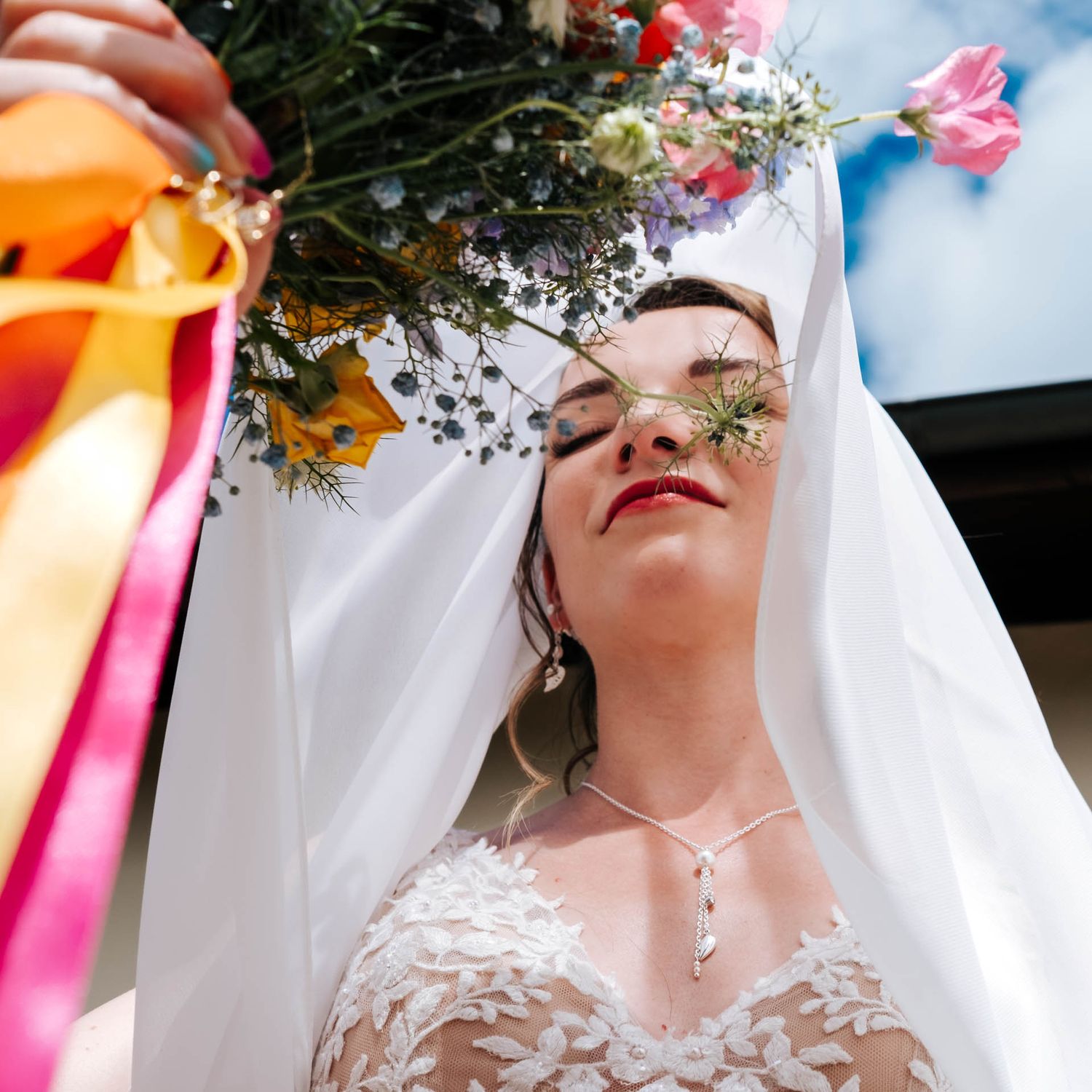 Delicate white flowers and greenery adorn a wedding veil against a soft blue sky background.