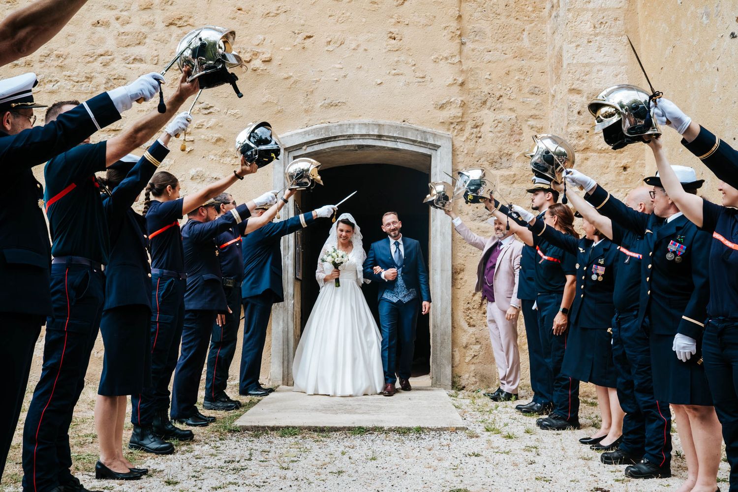 Military service members form an arch with swords for a traditional wedding ceremony exit.