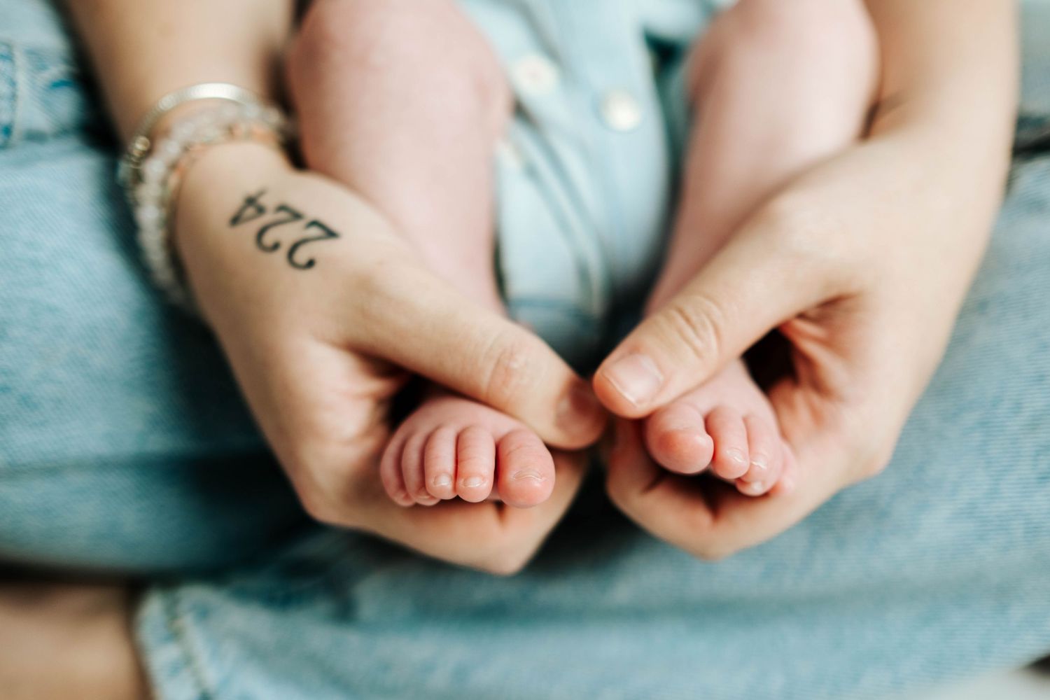 Close-up of adult hands gently holding tiny baby feet against soft blue fabric background.