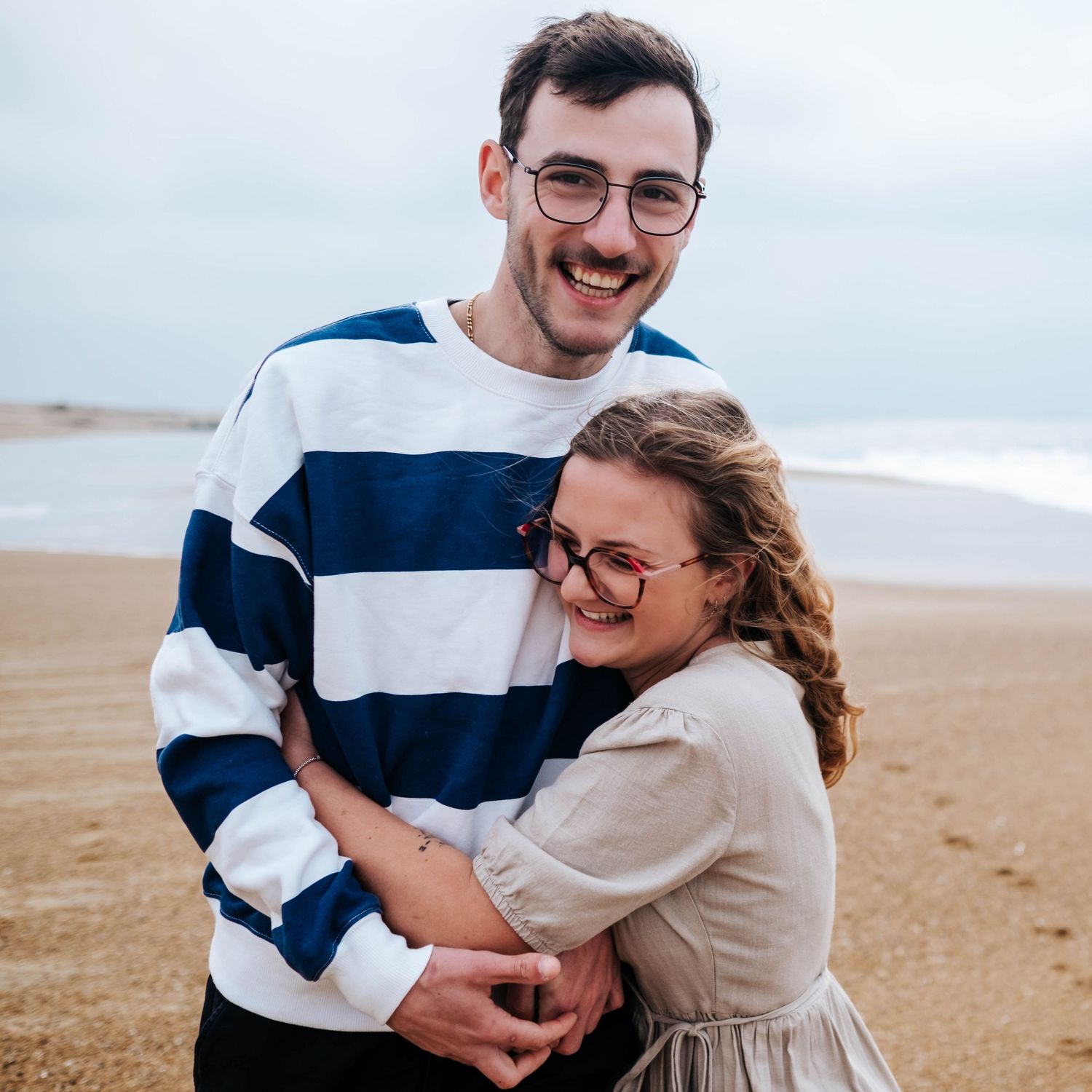 A couple shares joyful moments together on a sandy beach while wearing casual clothing and embracing.