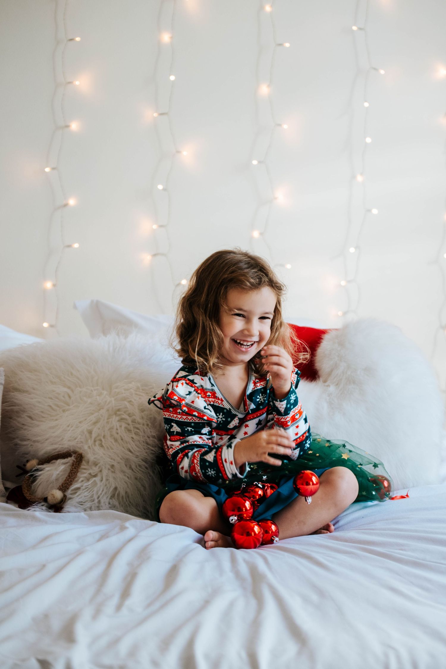 A series of photos showing a child in a floral dress lying on a white bed with fairy lights and plush decor in the background.