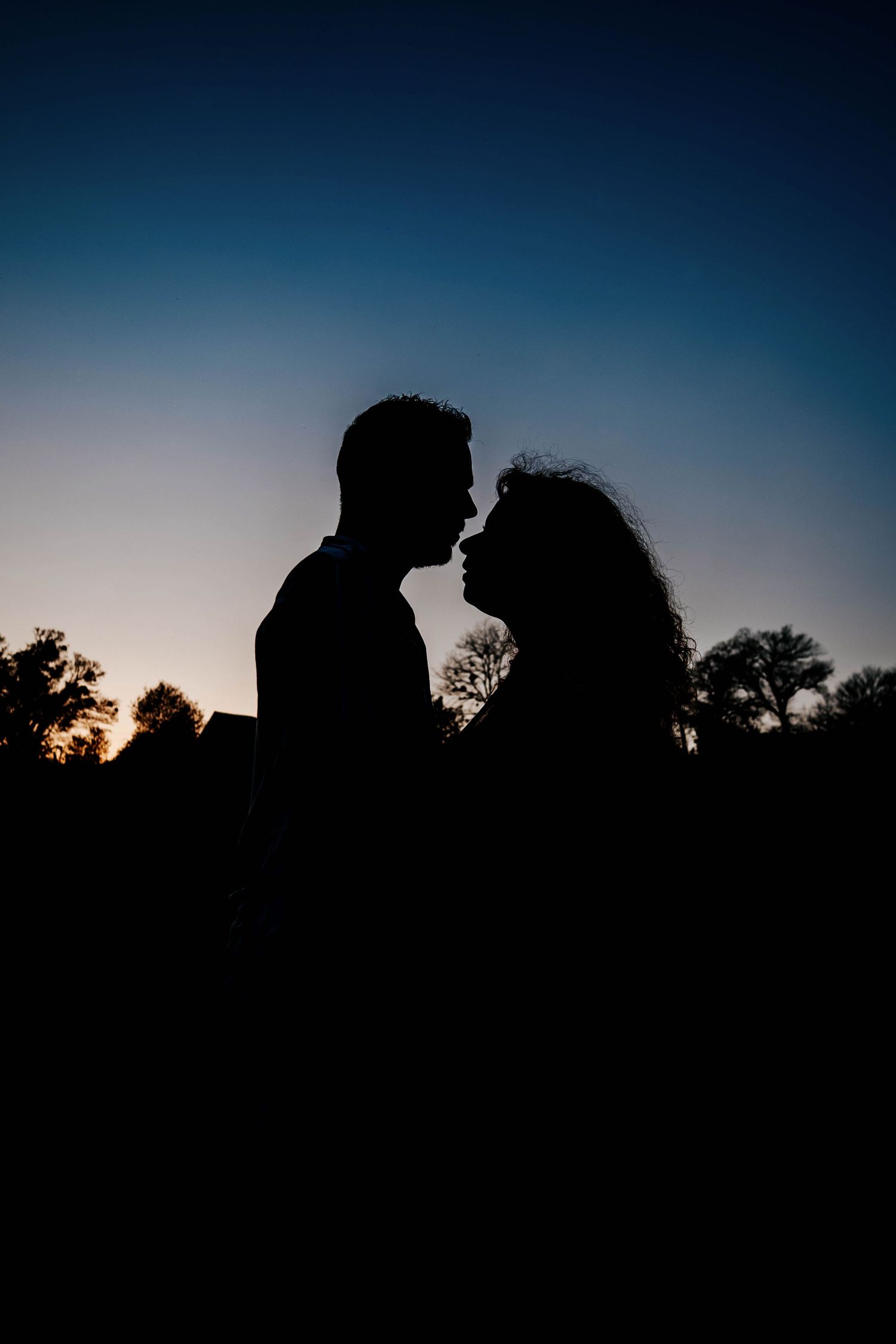 Romantic silhouette of a couple facing each other against a twilight sky at dusk.