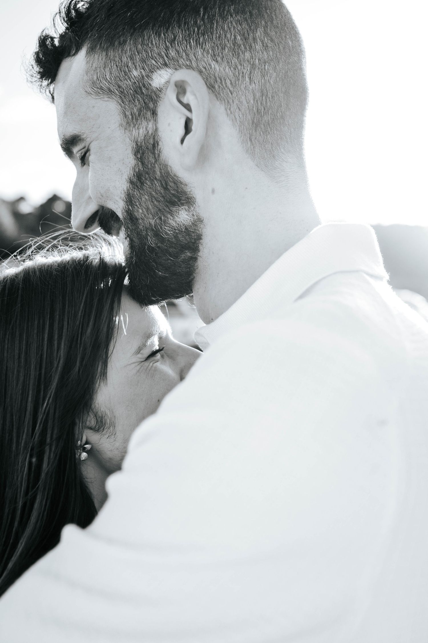 Black and white photo of a bearded man tenderly kissing a woman on the forehead in a romantic embrace.