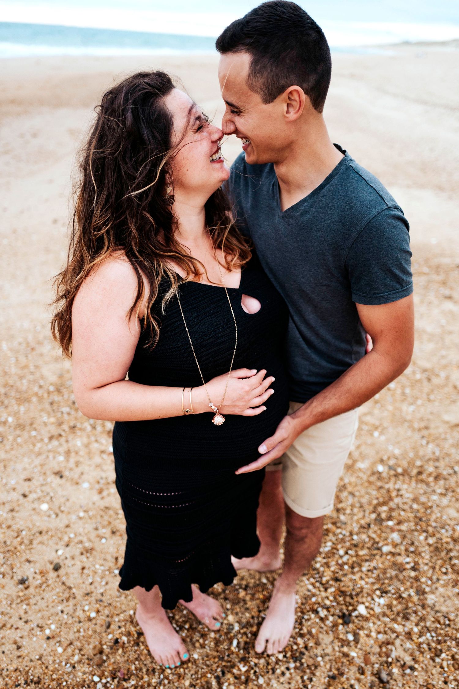 Romantic couple embraces and shares intimate moments on a pebble beach during sunset photoshoot.