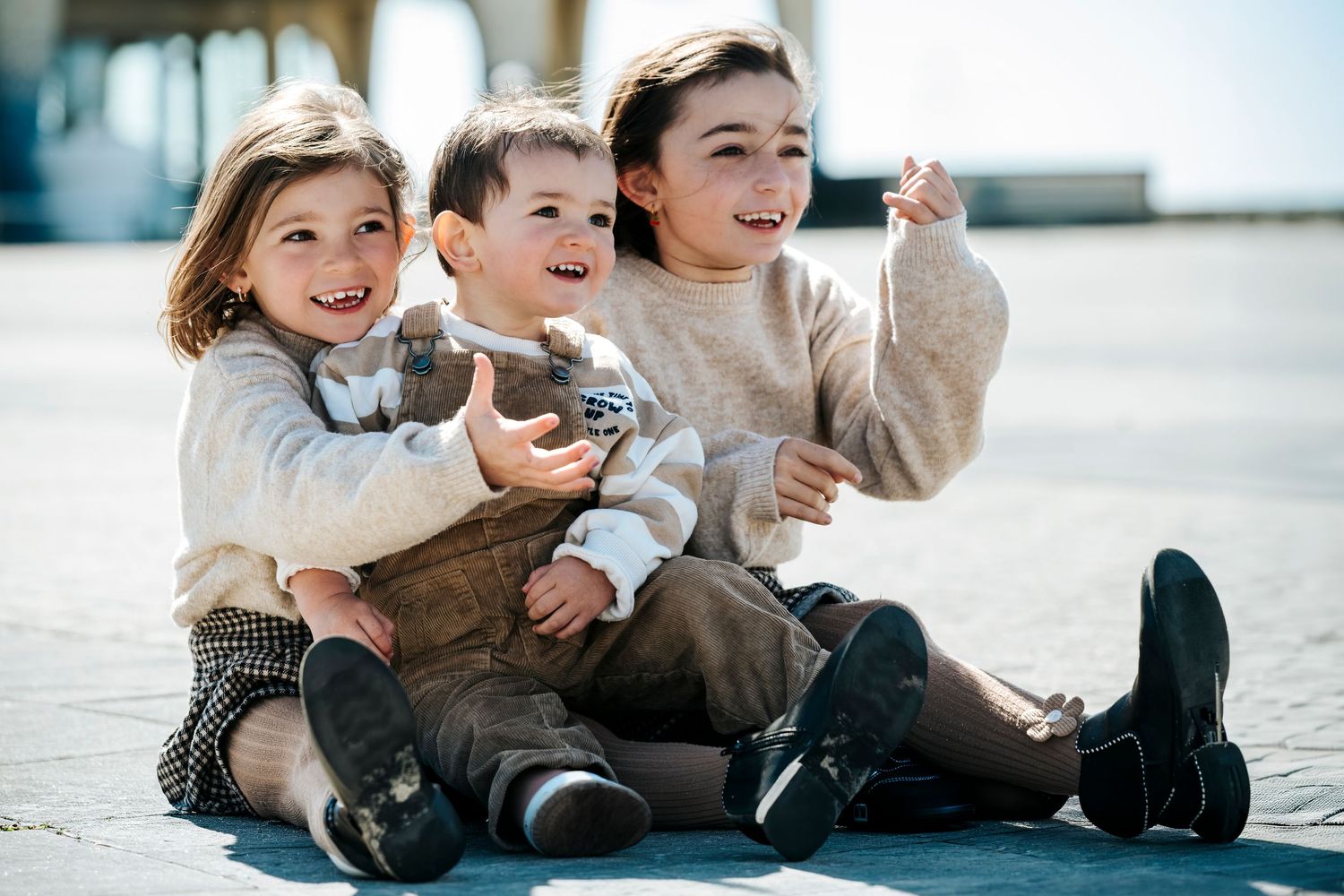 Three happy children sitting together outdoors, smiling and laughing on a sunny day.