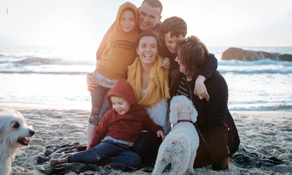A family and their white dog share joyful moments together on a scenic beach at sunset.