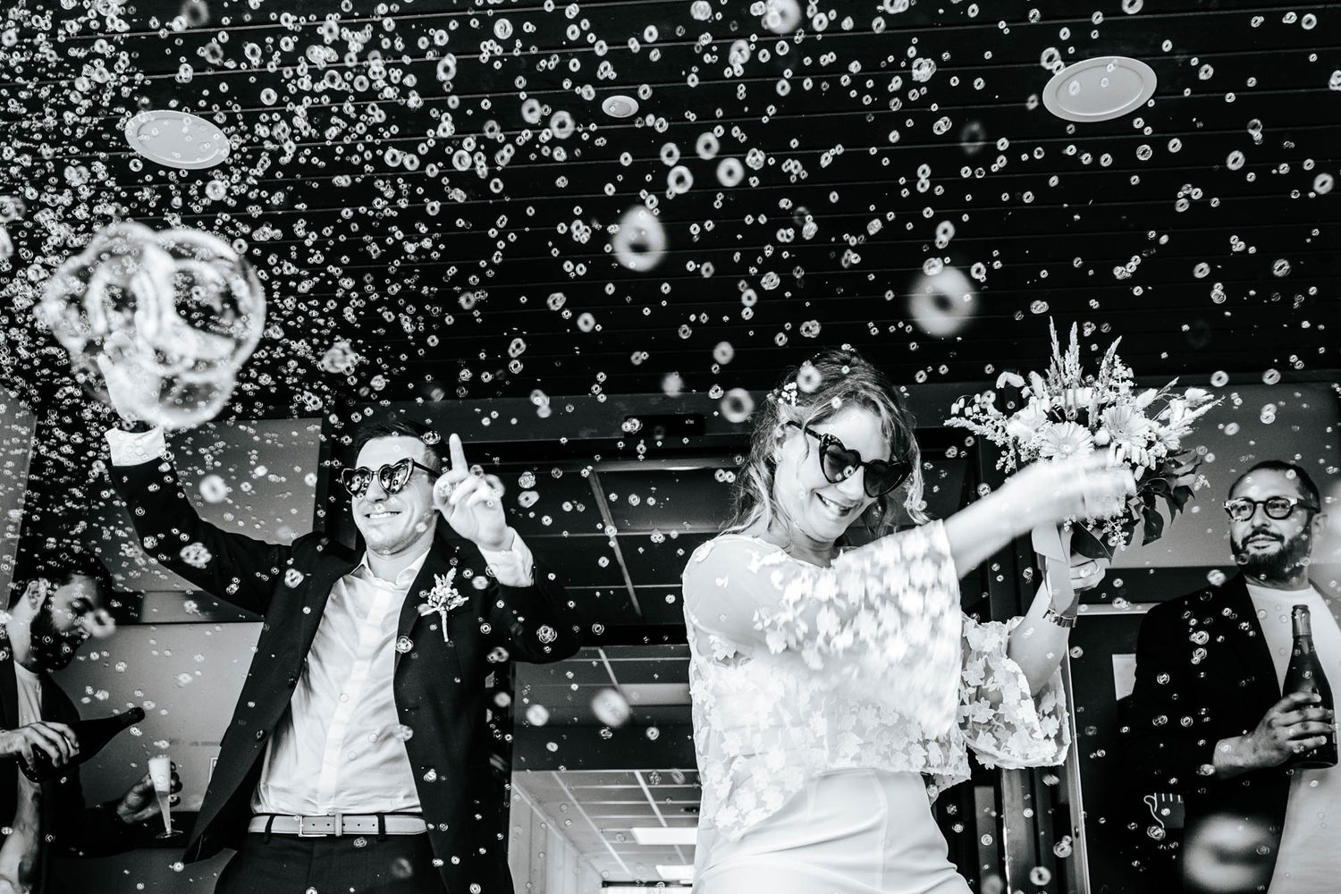 Black and white photo of performers on stage spraying champagne during an energetic celebration with bubbles in the air.