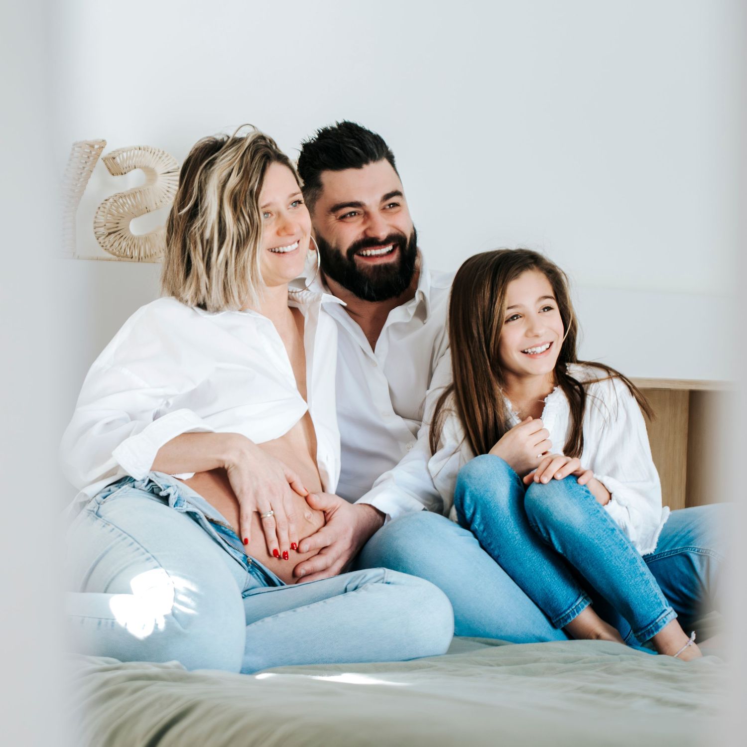 Happy family with young child relaxing together on bed in casual home setting with natural light.