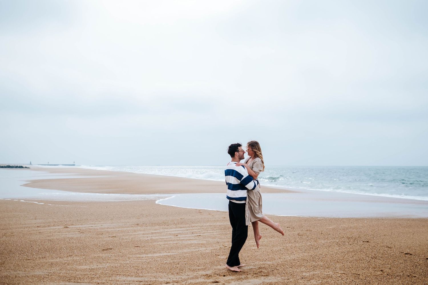 A couple embraces on a misty beach shoreline during what appears to be a romantic photoshoot session.