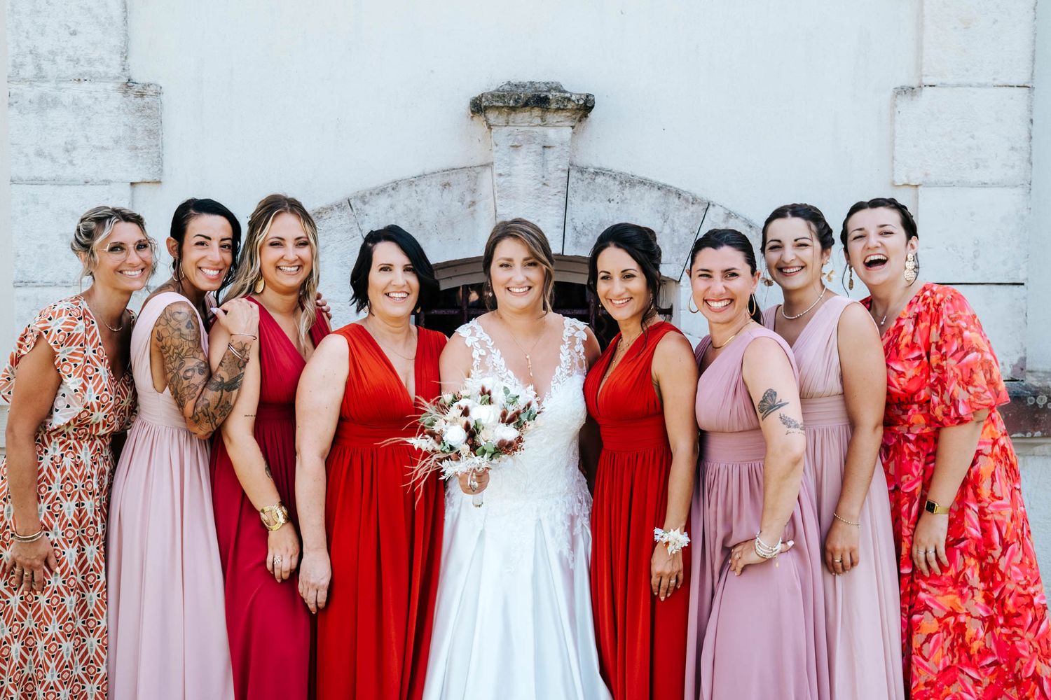 Bridesmaids in pink and red dresses pose together for a wedding party photo.