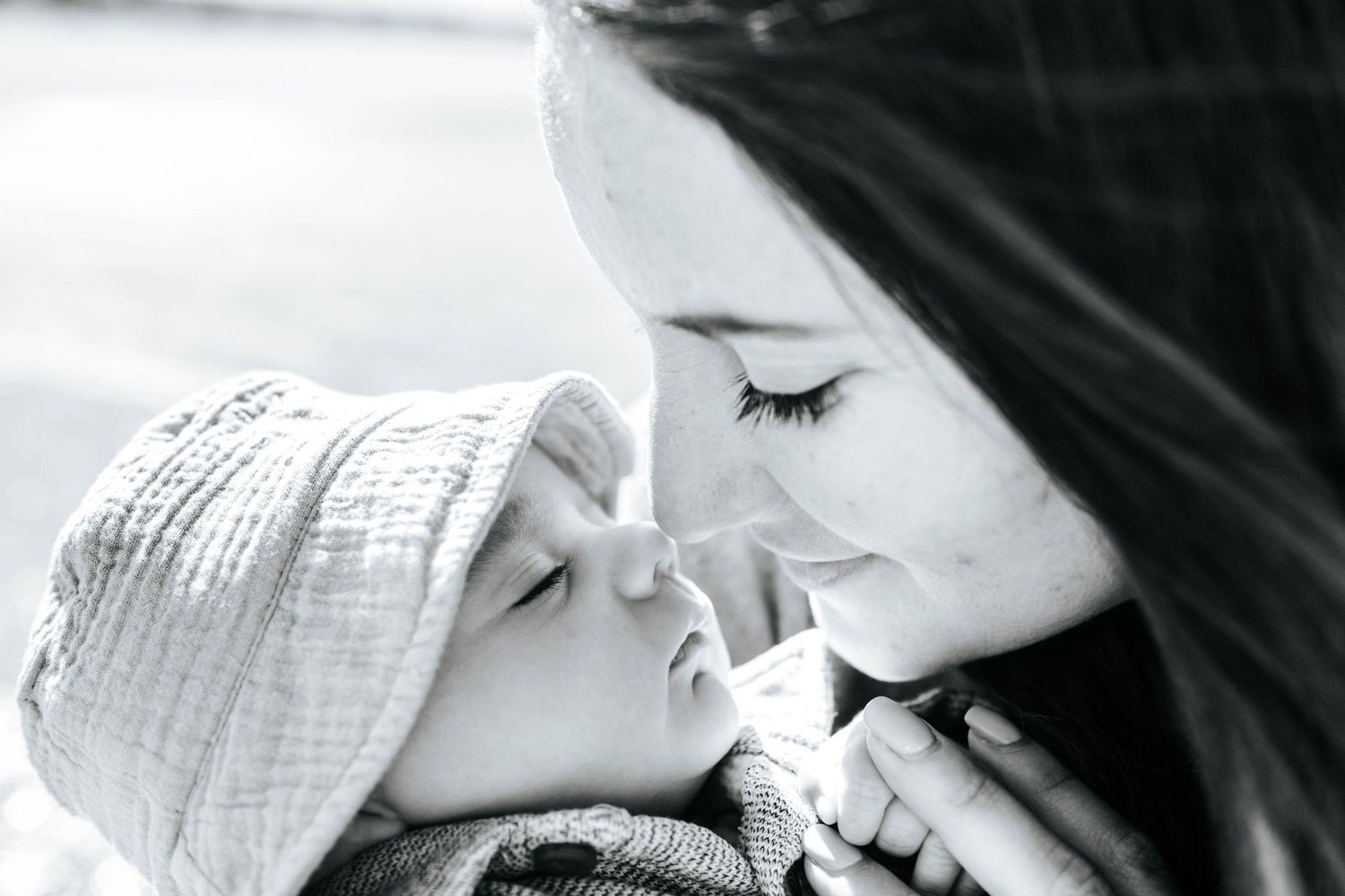 Black and white close-up photo showing tender moment between parent and child in winter hat.