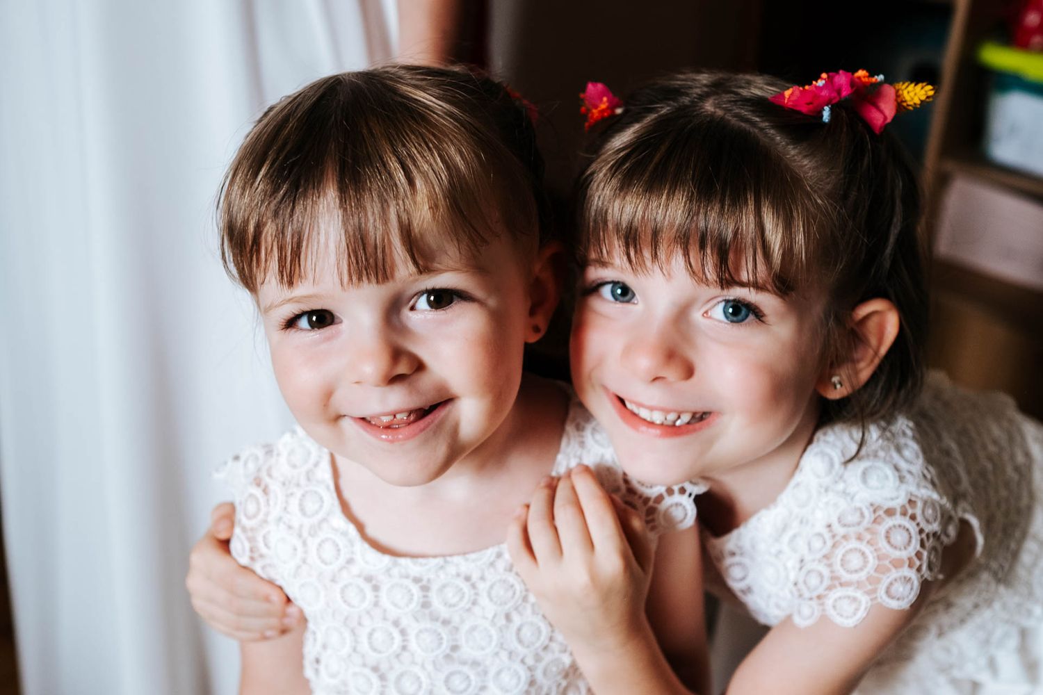 Two young girls in matching white lace dresses pose together.