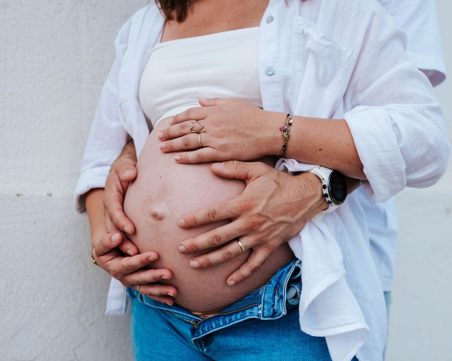 A pregnant woman in blue jeans and white shirt holds her growing belly in a maternity photoshoot sequence.