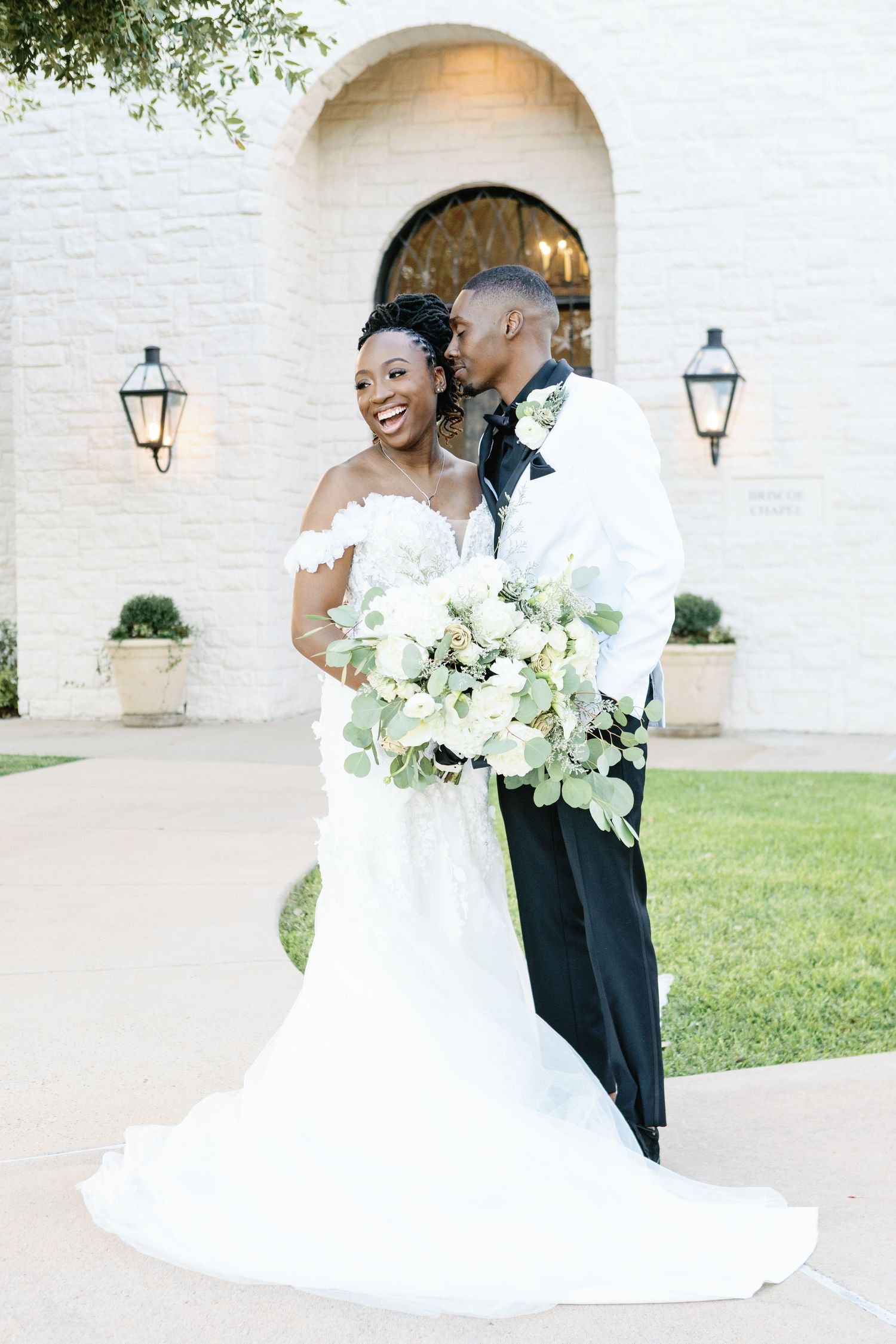 A romantic wedding couple shares intimate embraces and laughter in front of a white stone wall with lanterns.