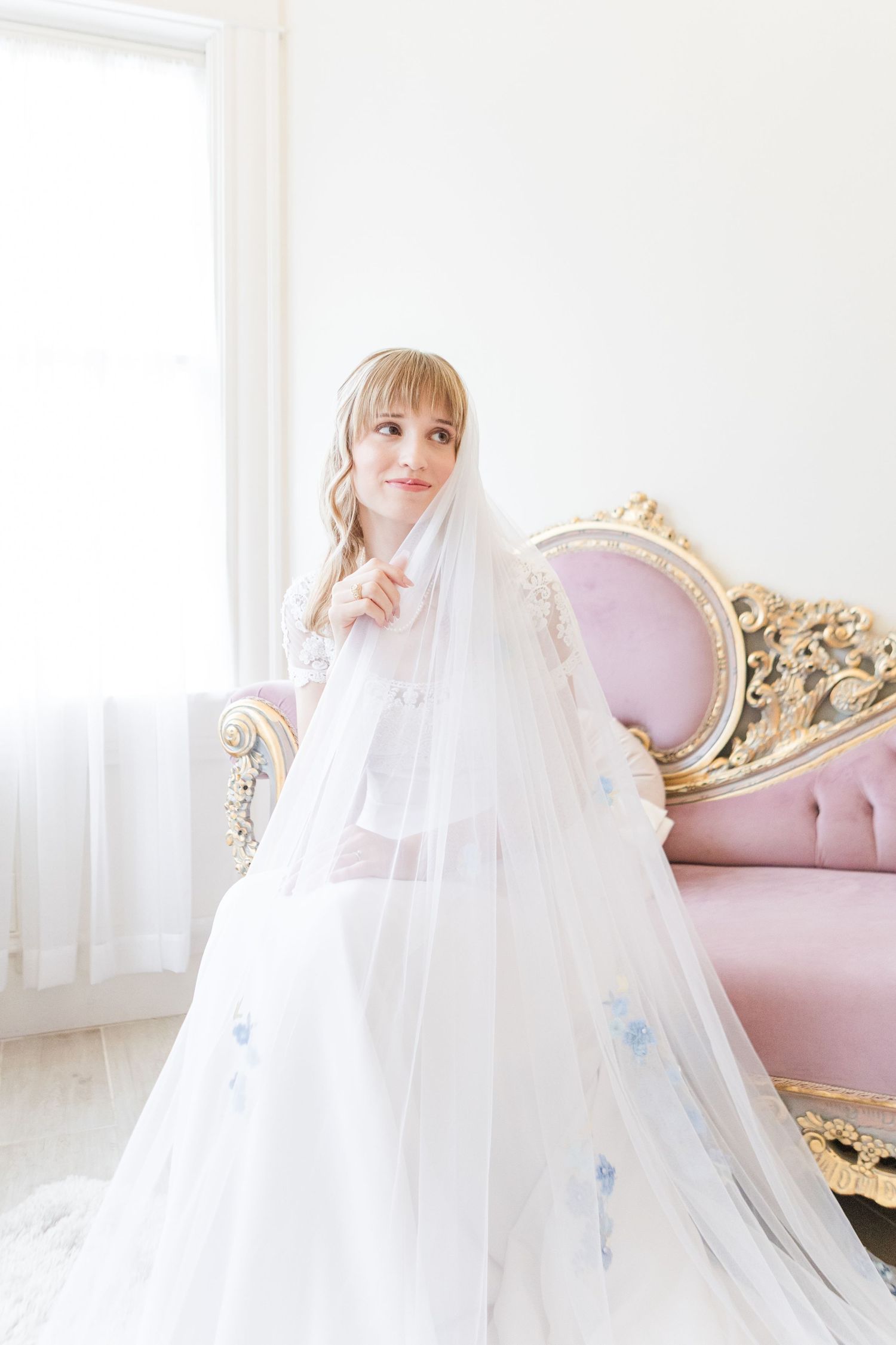 Dreamy bridal portrait with sheer veil against luxurious pink furniture.