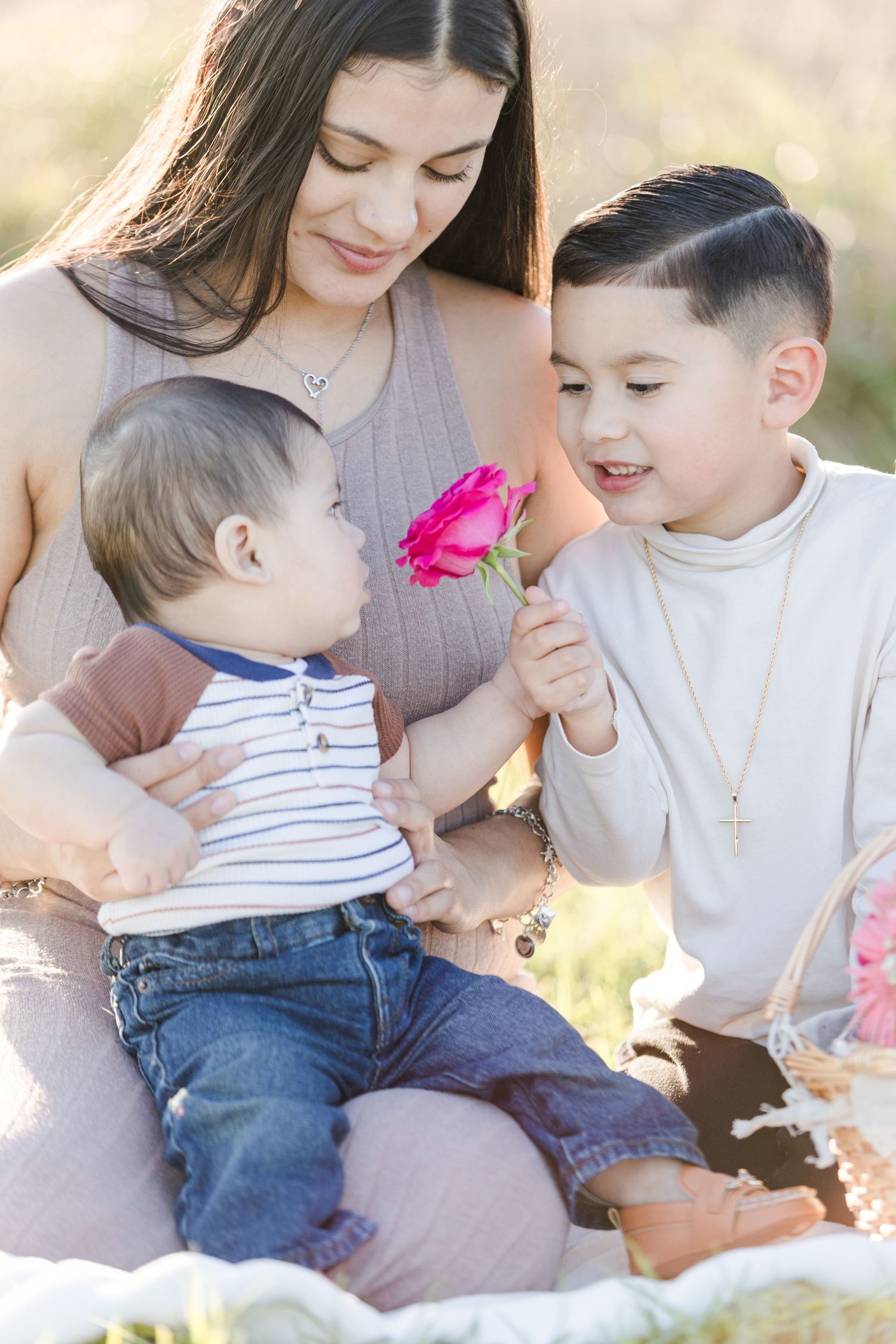 A tender moment is captured outdoors with pink flowers and casual attire in warm sunlight.