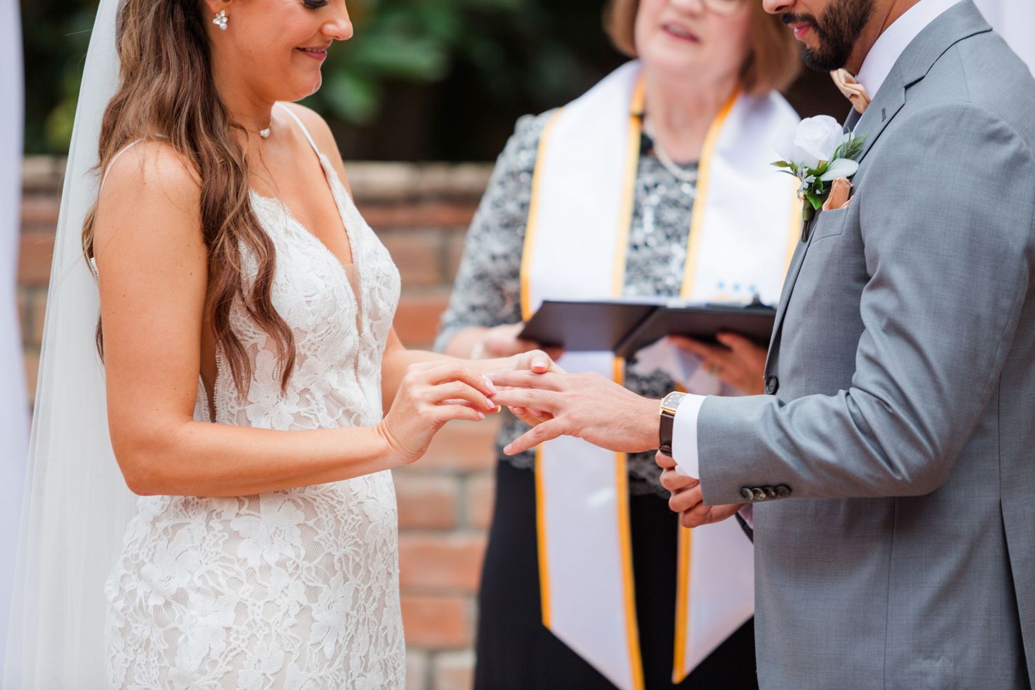An intimate outdoor wedding ceremony takes place under a decorated white arch.