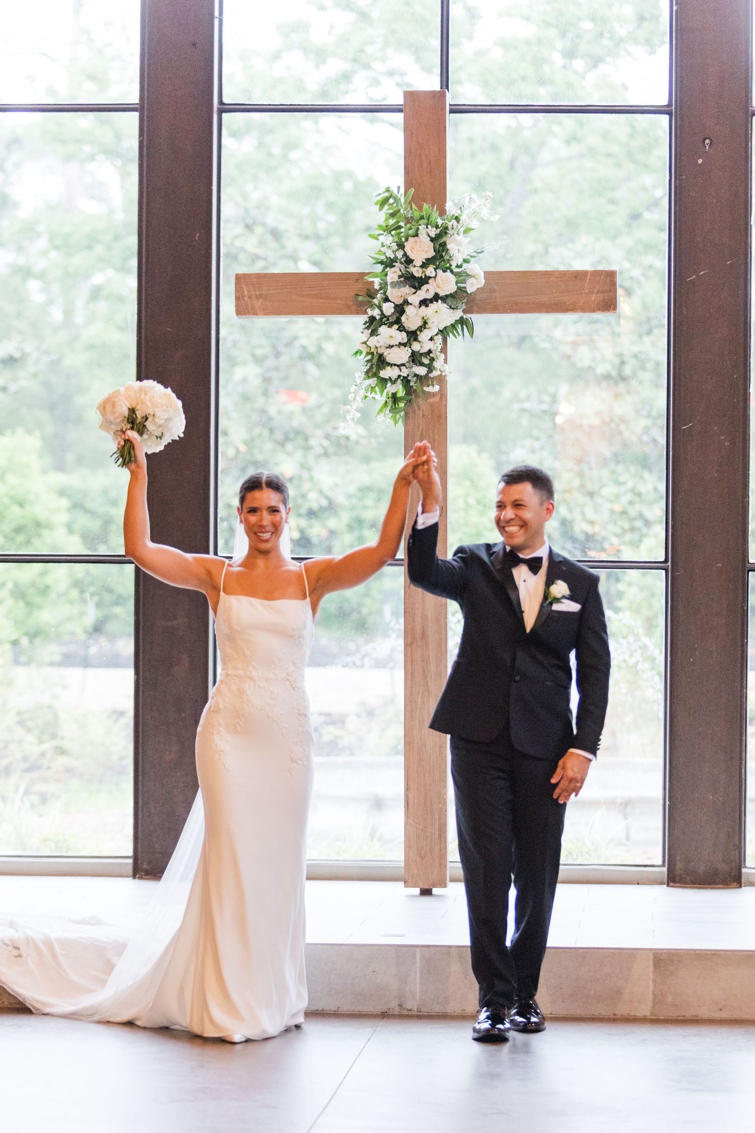 Newlyweds celebrate with raised arms after their wedding ceremony in a light-filled venue.