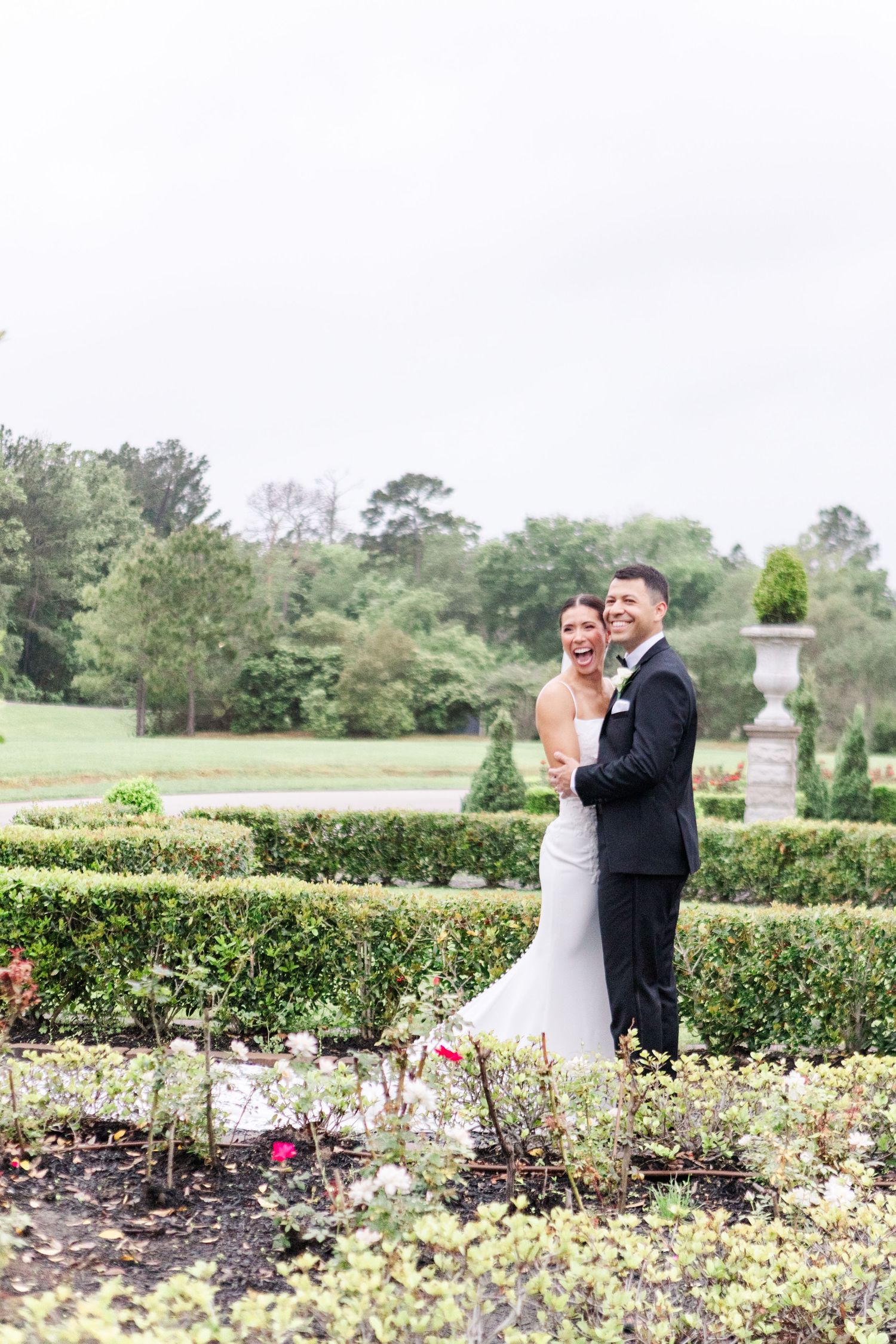 Couple shares intimate moment in formal attire among manicured garden hedges.