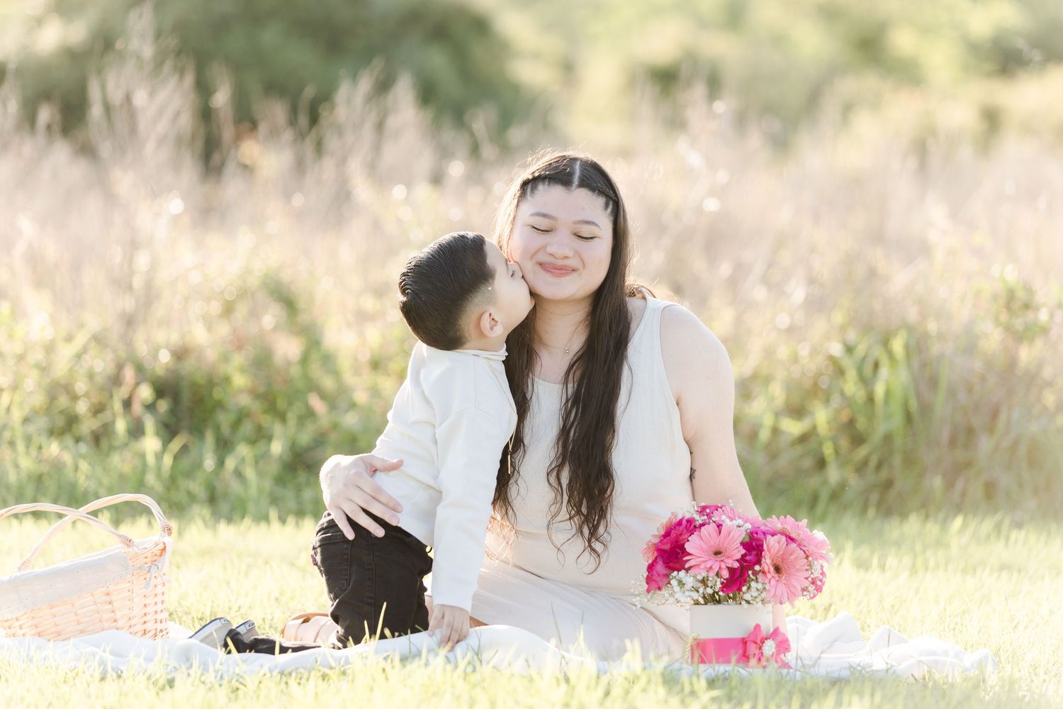 Sun-drenched maternity photos in natural field setting with pink flowers.