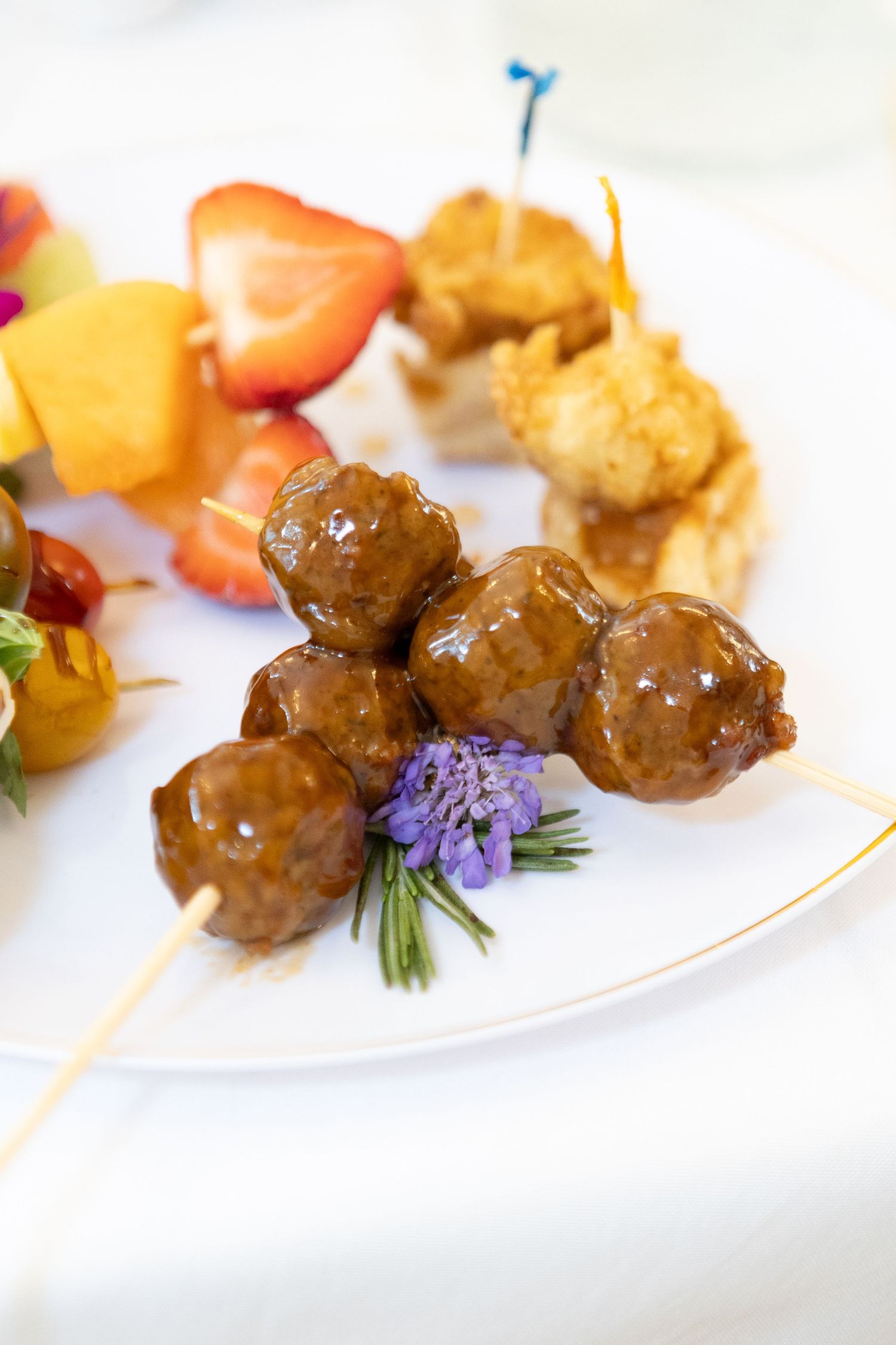 Small glazed meatballs garnished with purple flowers and herbs served as elegant appetizers on white plates.