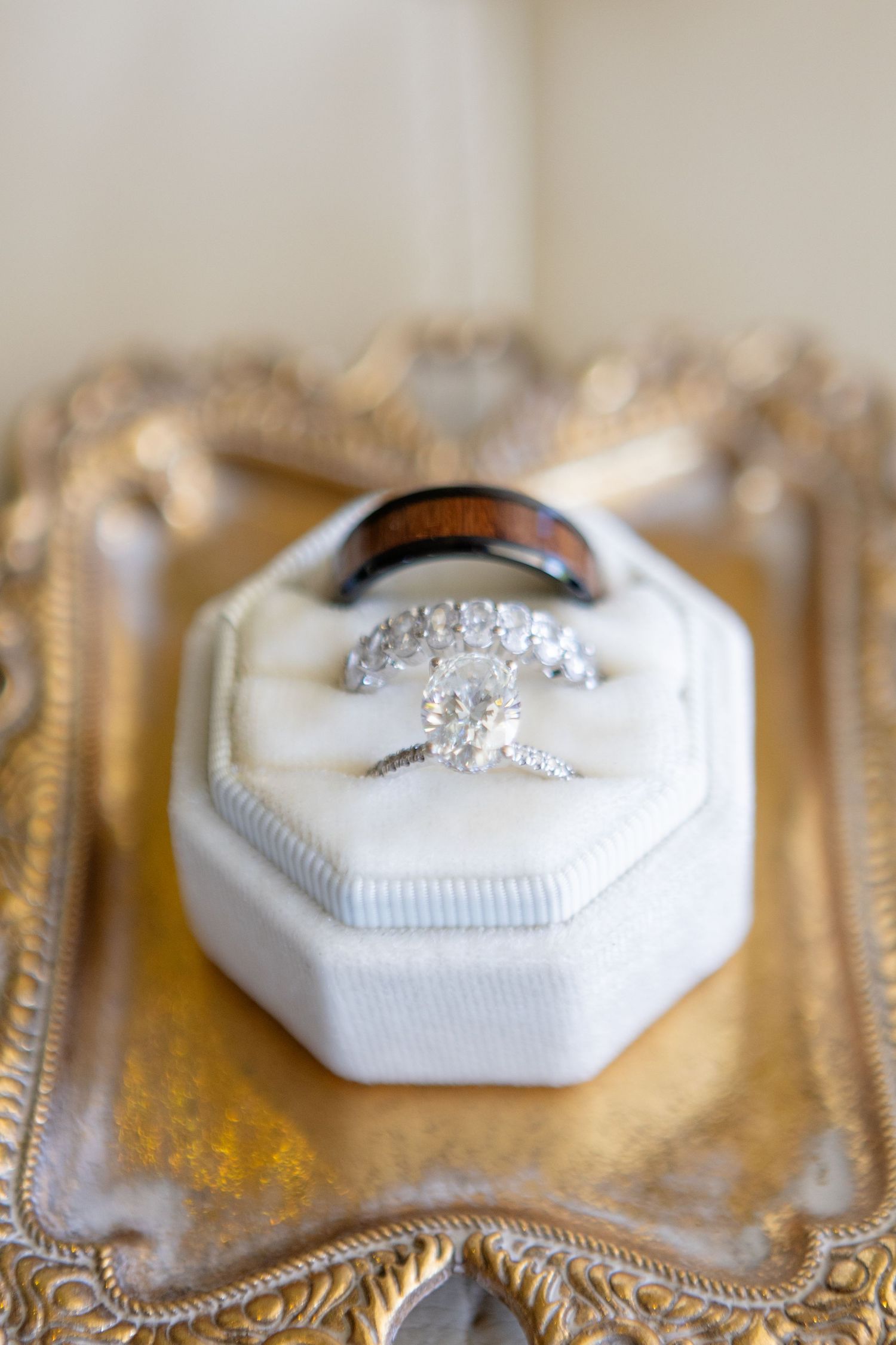 Diamond engagement ring sitting in white hexagonal ring box on ornate gold tray.