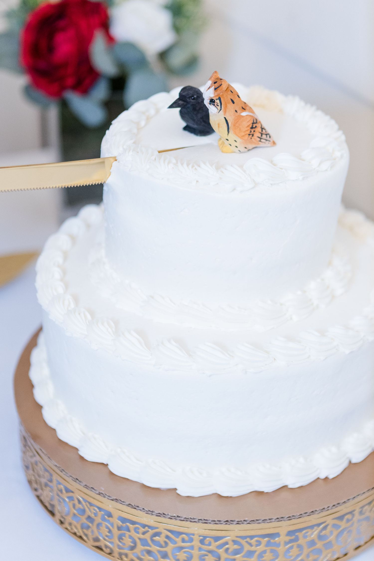 White wedding cake decorated with cat cake toppers on a gold-accented stand.