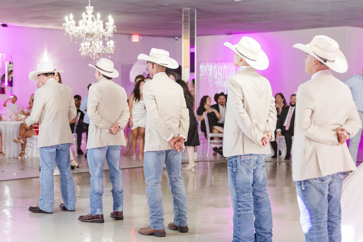 Line of guests in white cowboy hats and jackets at a celebration in a purple-lit ballroom.