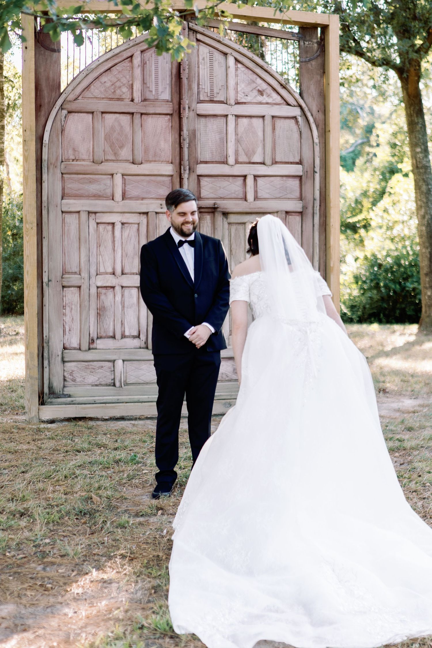 Wedding couple shares their first look moment in front of weathered pink doors at an outdoor venue.
