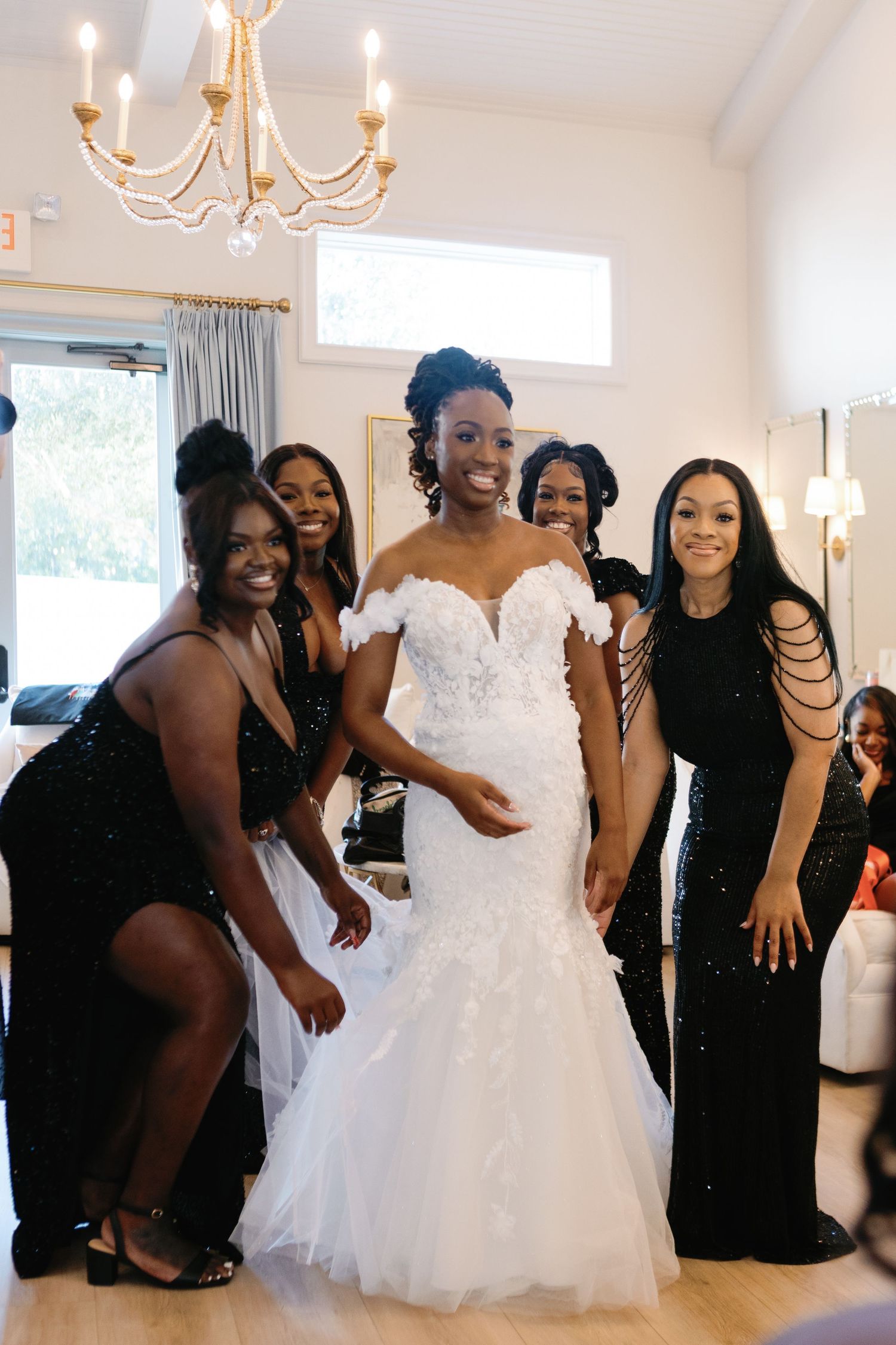 Wedding party celebrating in a bright room with chandelier and white walls.