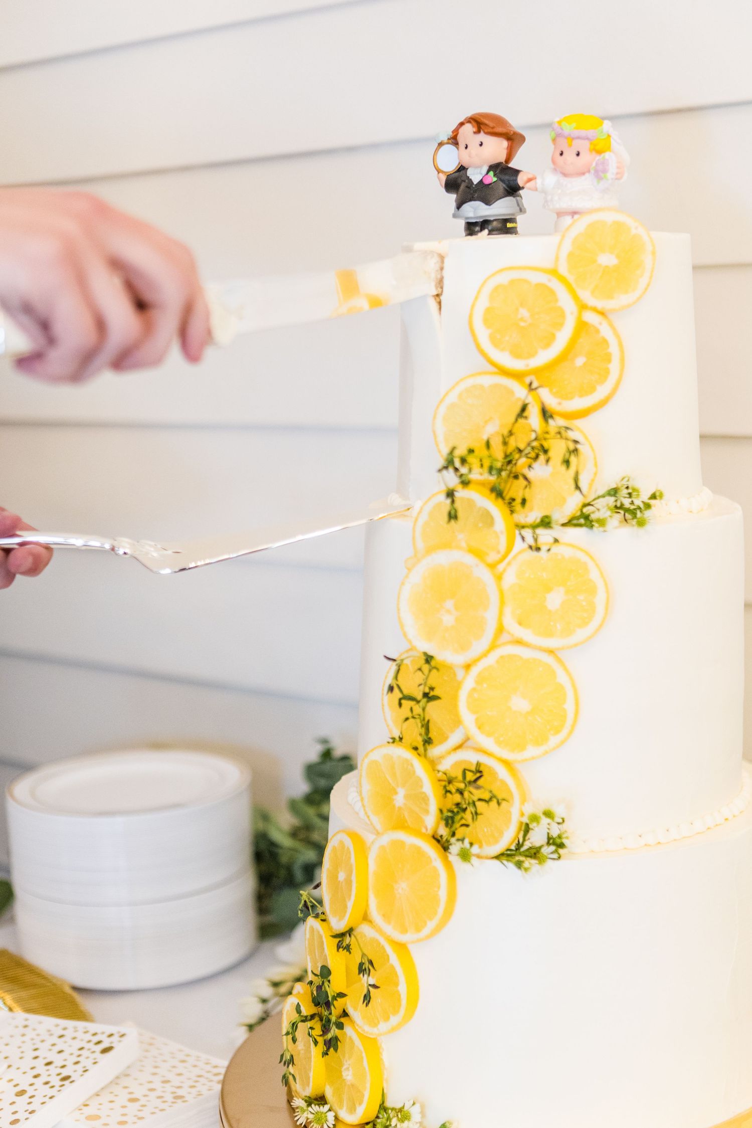 Three-tiered white wedding cake adorned with fresh lemon slices and herbs.