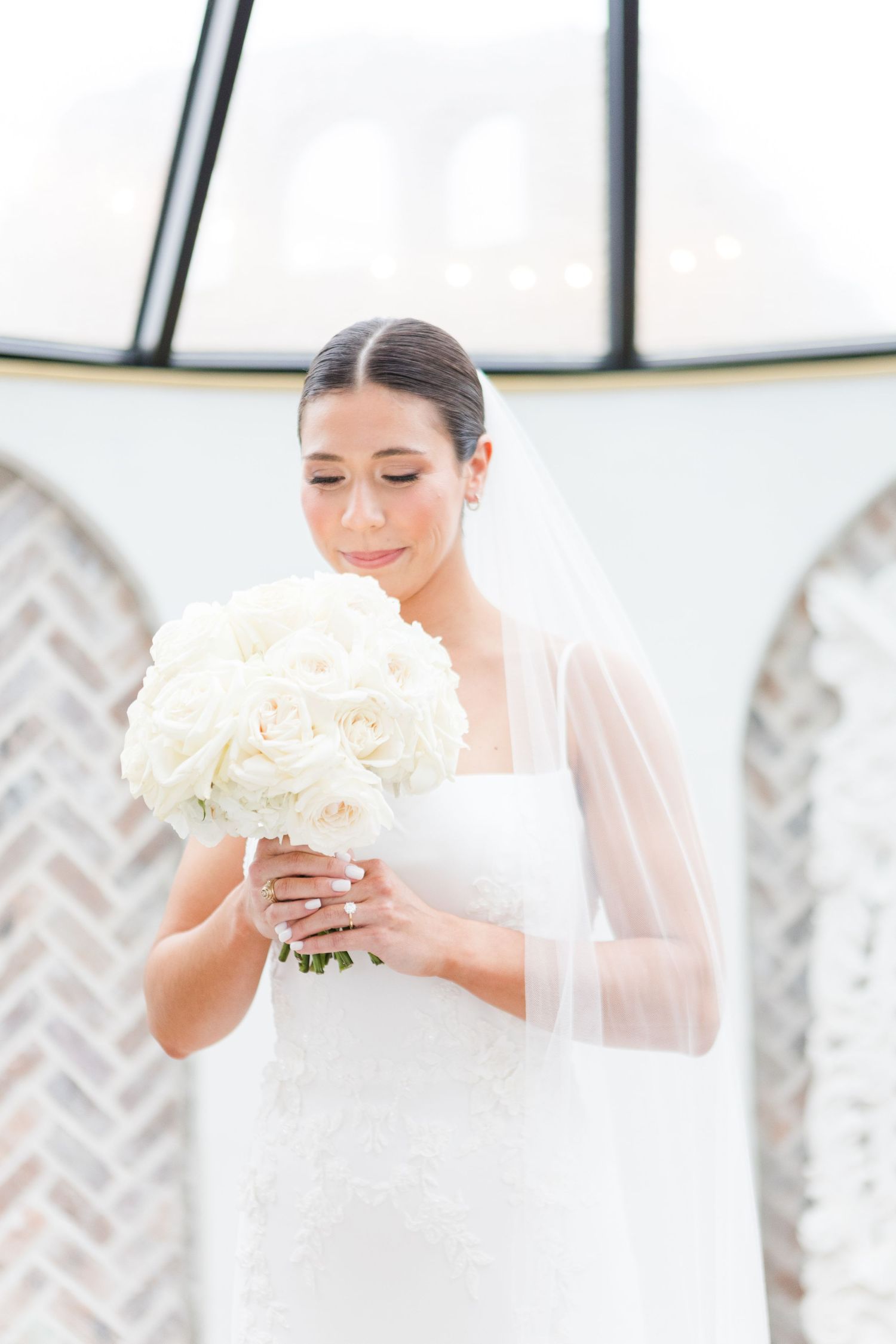 Elegant wedding scene showing bride holding a classic white rose bouquet in a light-filled room.