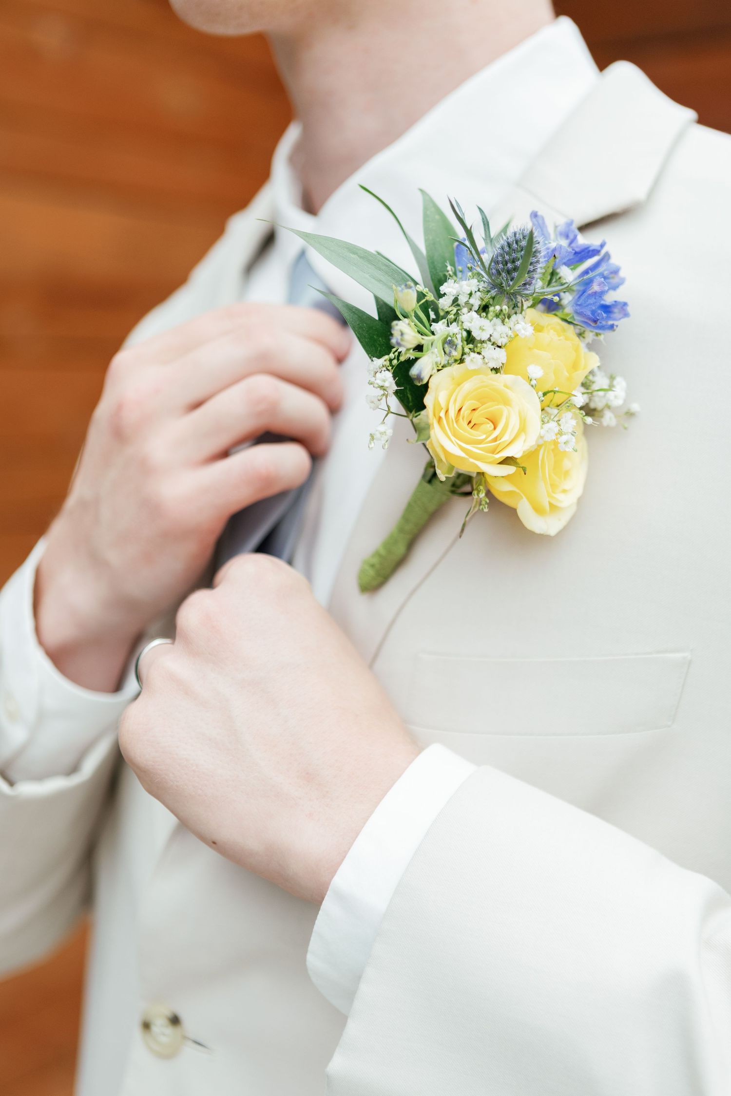 Wedding party member pins yellow rose and blue flower boutonniere to white suit jacket.