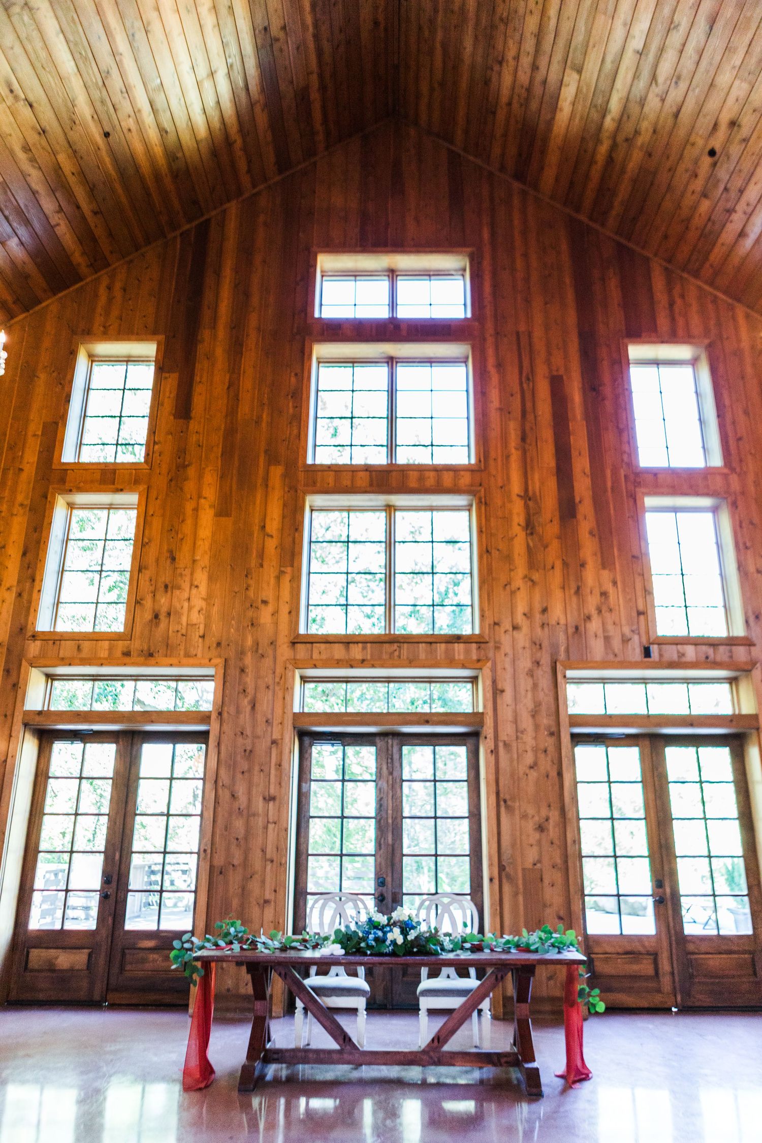Interior of a wooden barn venue with high ceilings and large windows letting in natural light.