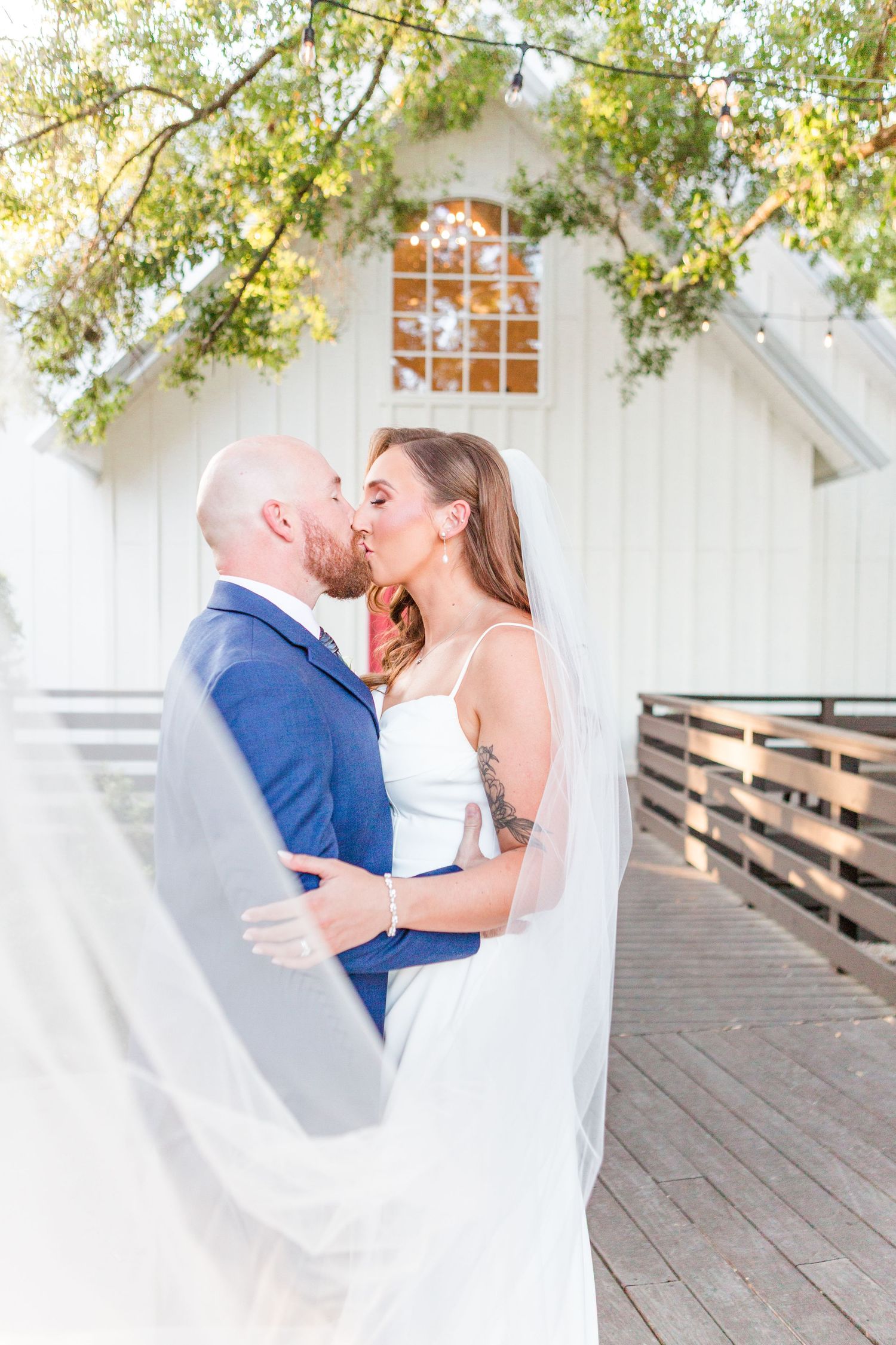Romantic moment on a wooden deck with rustic barn buildings in the background.