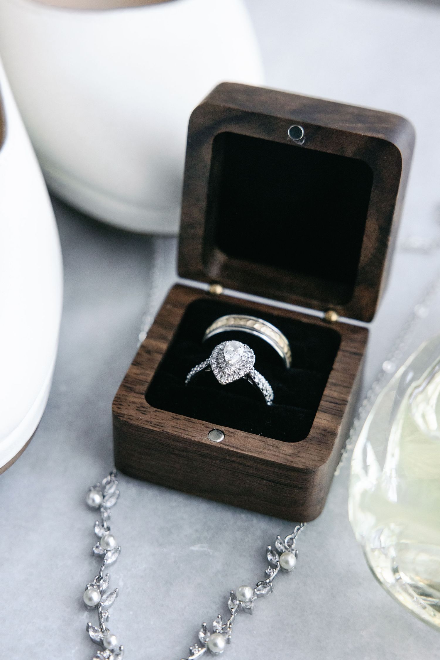 Diamond engagement ring shown in a dark wooden box with matching earrings on a light gray surface.