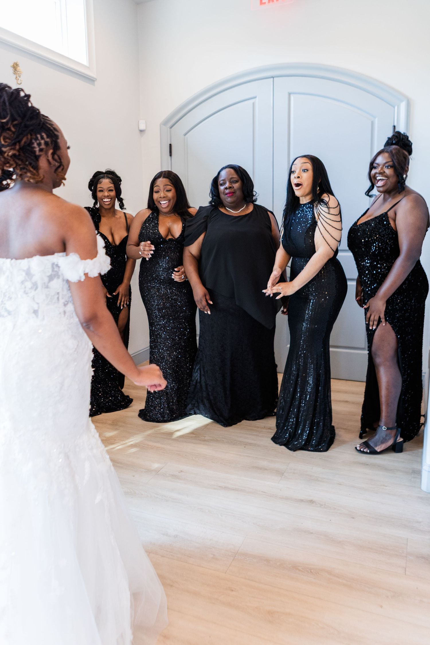 Bridesmaids in black sequin dresses gather with bride in white gown.