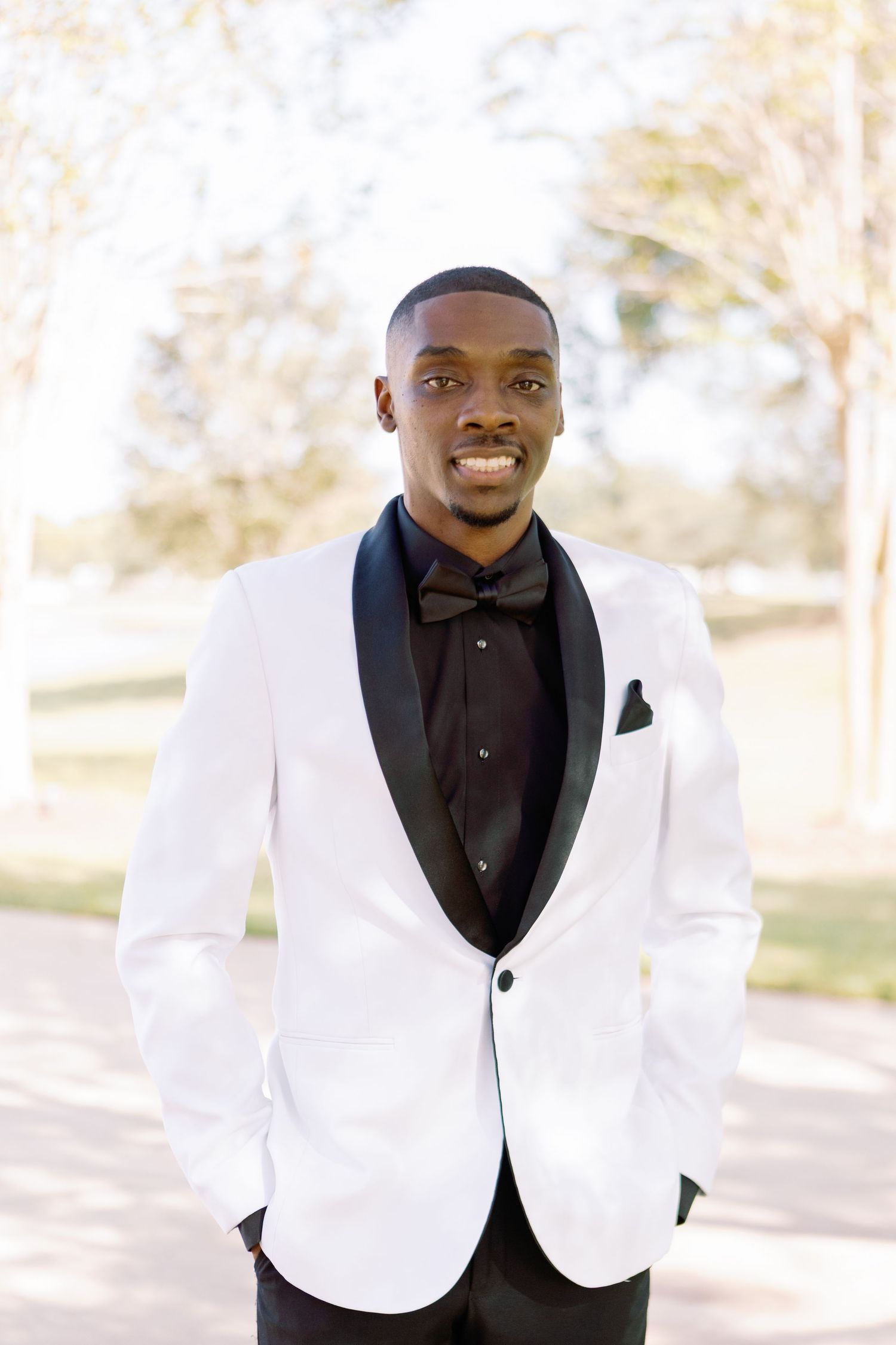 Professional portraits showing a man in a crisp white tuxedo jacket and black shirt smiling in an outdoor setting.