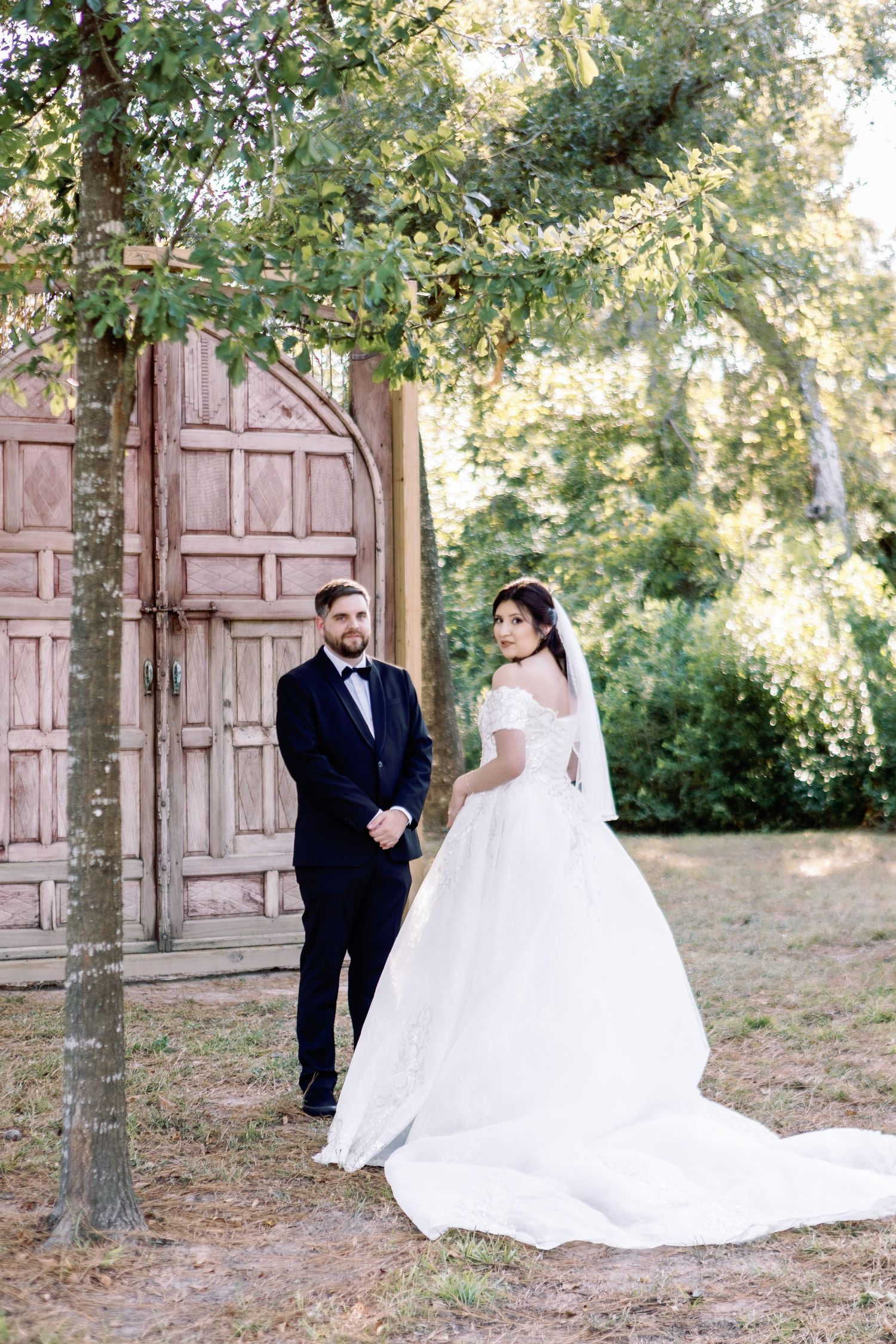 Elegant wedding couple poses in a garden setting with vintage wooden doors as a backdrop.