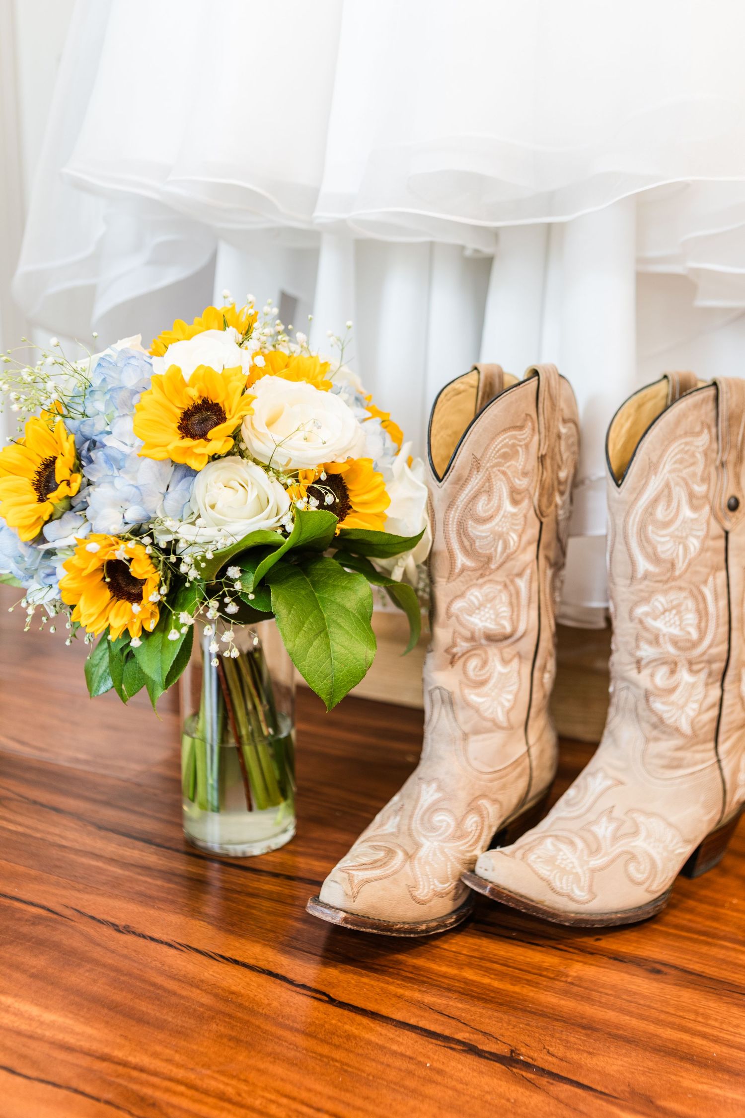 Tan cowboy boots and sunflower bouquet arrangements displayed on wooden floor.