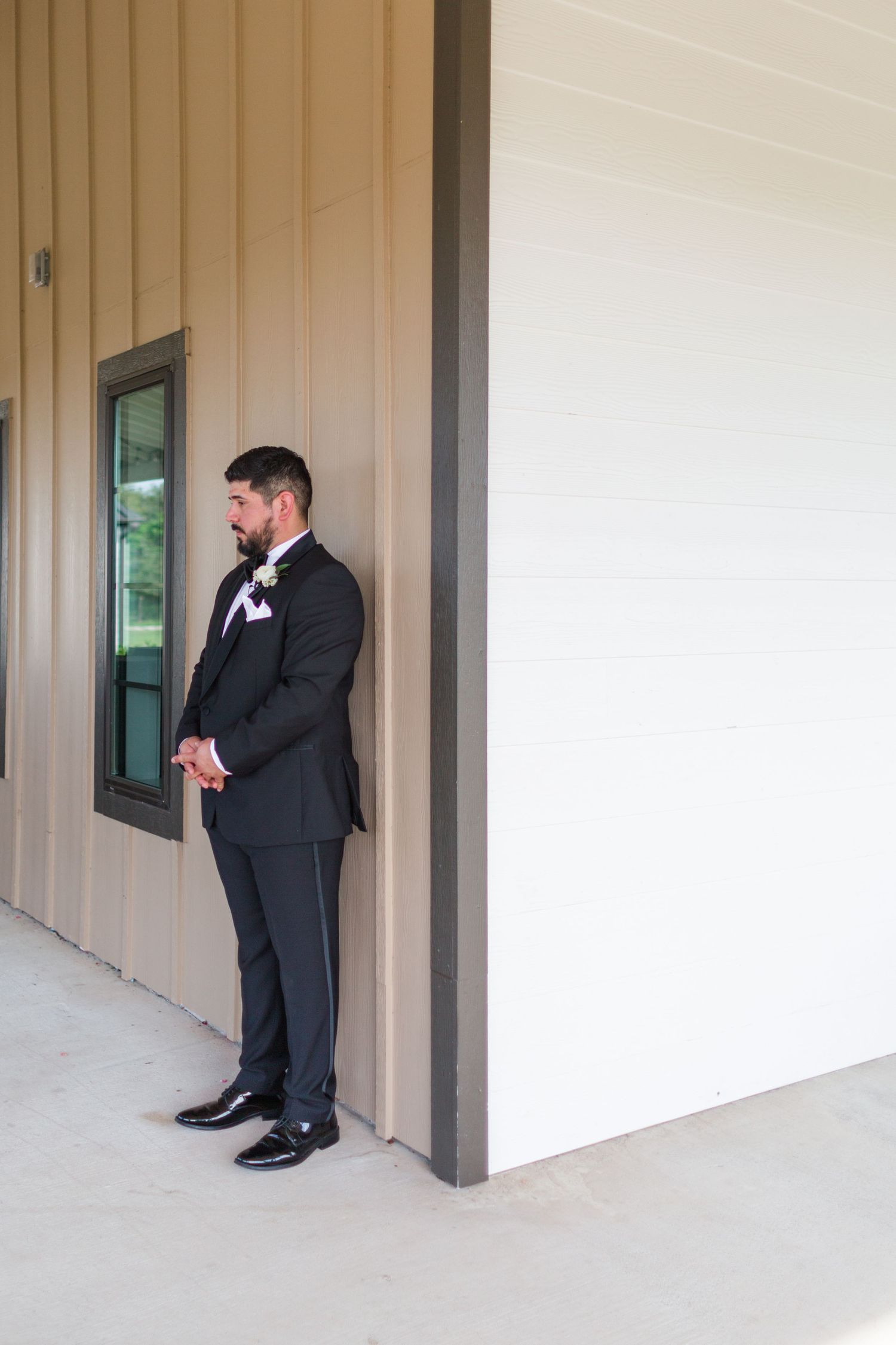 Groom in classic black tuxedo waiting patiently during first look wedding moment.