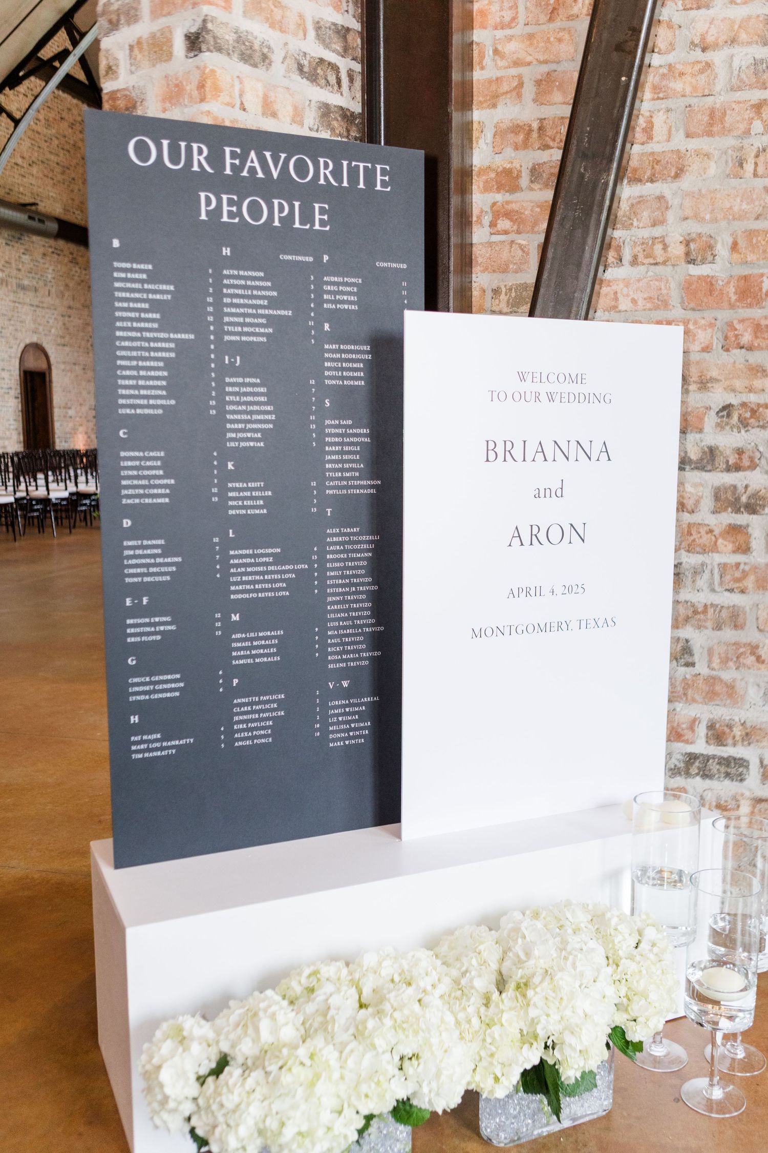 Modern wedding seating chart and welcome signs displayed on gray and white boards with floral accents.