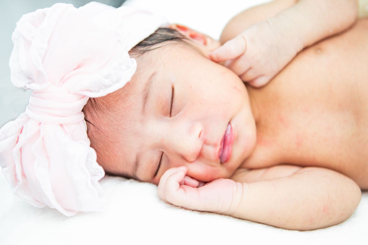 Peaceful newborn photography session with soft white and pink tones against light background.